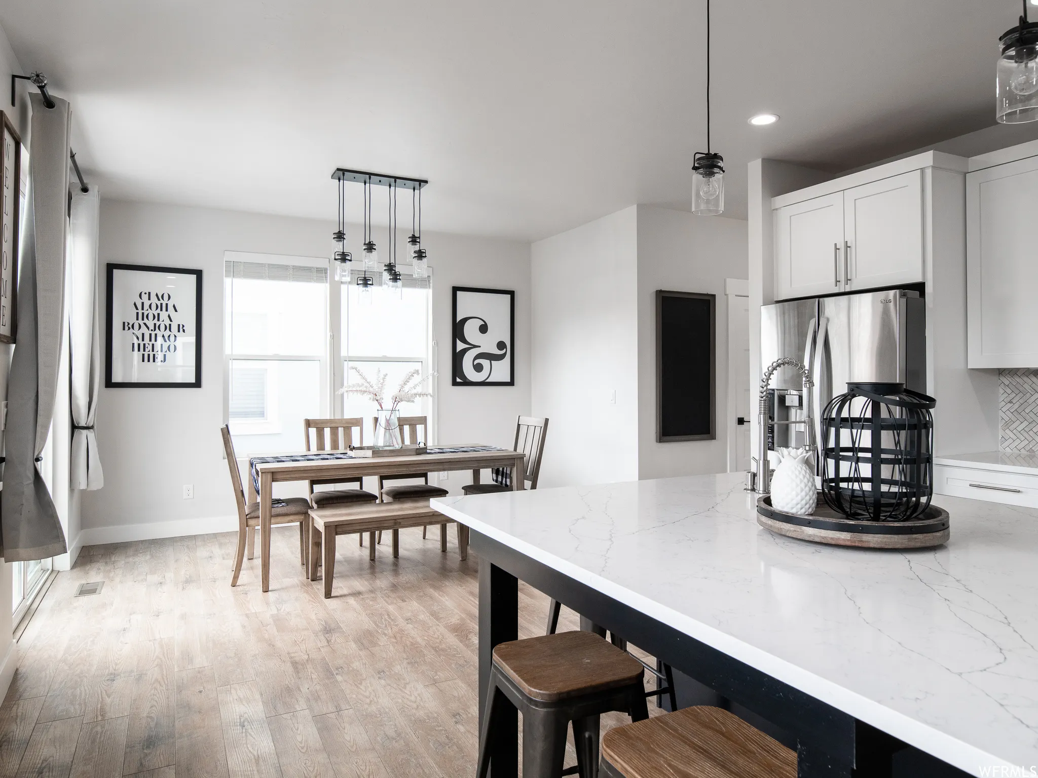 Kitchen featuring a breakfast bar, decorative light fixtures, stainless steel fridge, light wood finished floors, and white cabinets
