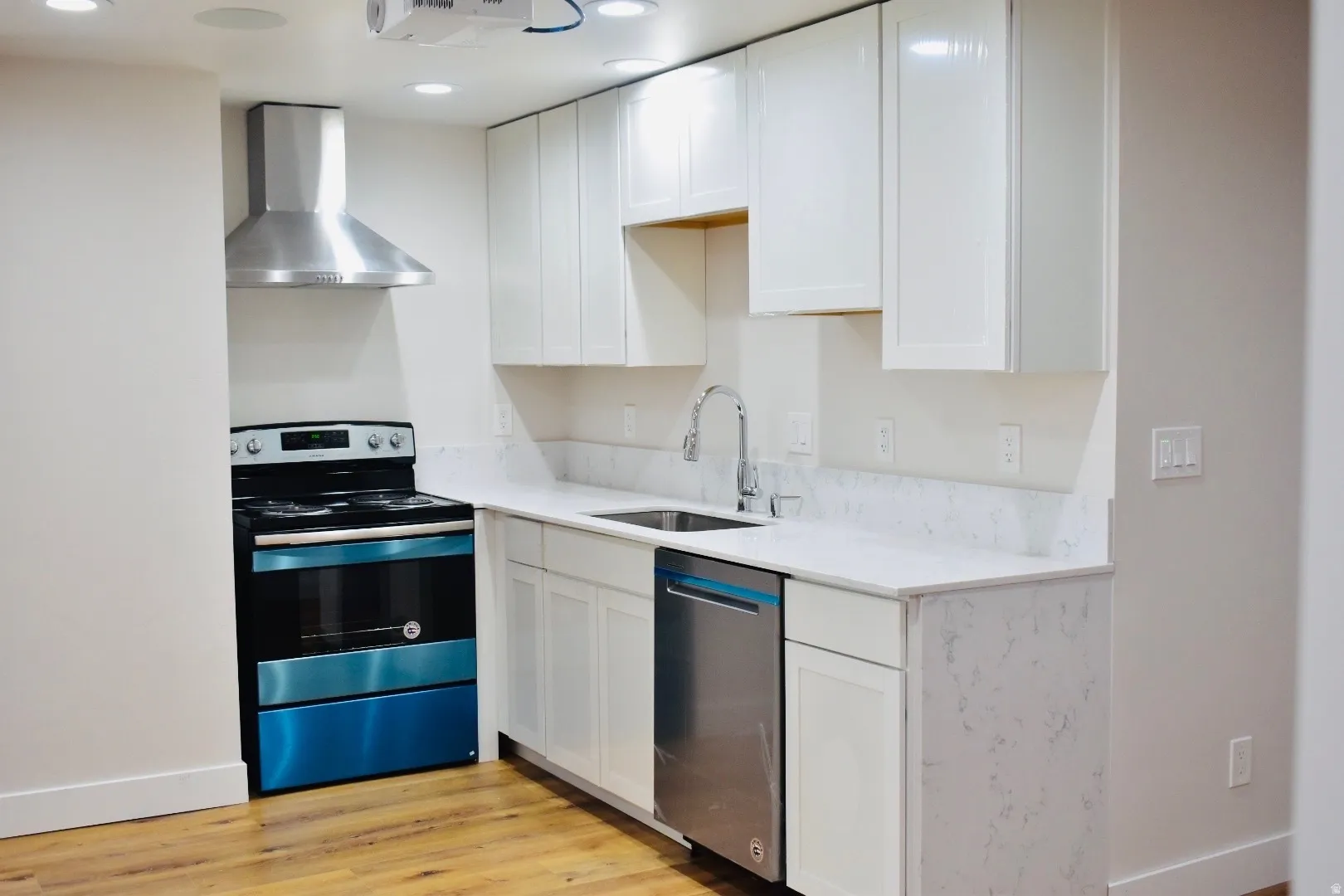 Kitchen with stainless steel appliances, white cabinets, light wood-type flooring, light stone countertops, and recessed lighting