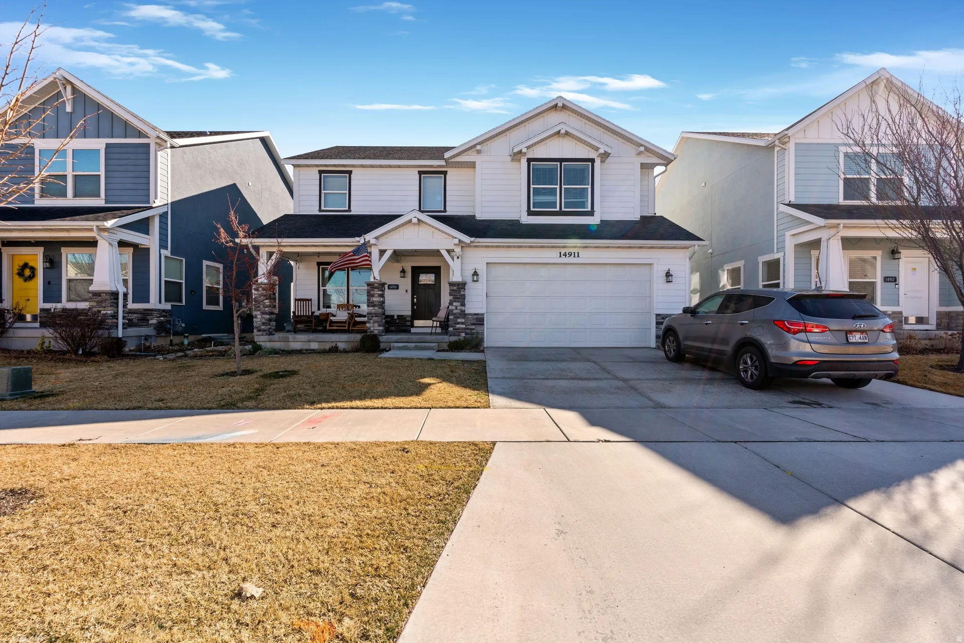View of front of home featuring covered porch, concrete driveway, an attached garage, a front lawn, and stone siding