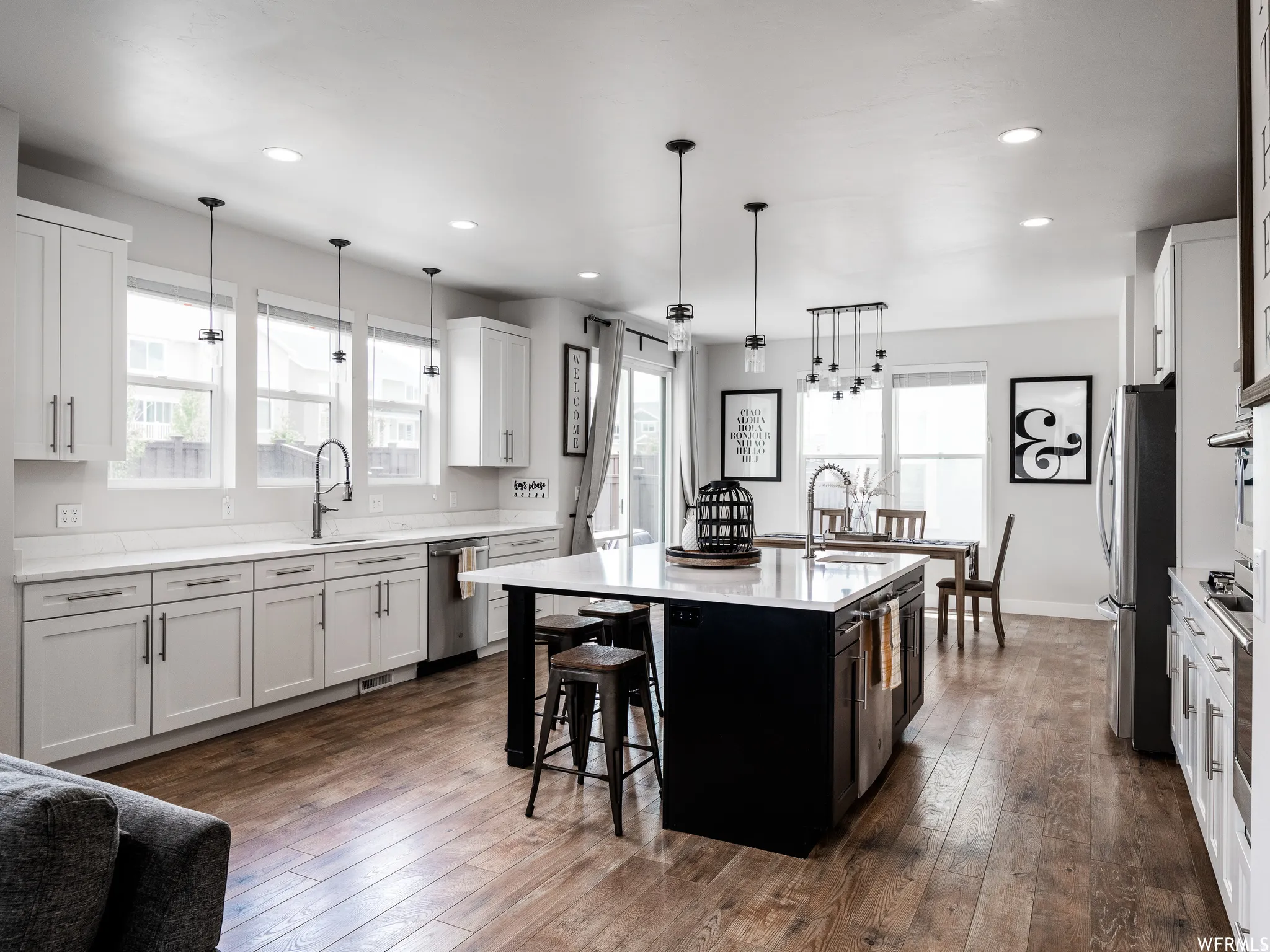 Dual tone kitchen featuring a center island with sink, dark wood finished floors, two tone cabinetry, light stone counters, and hanging light fixtures