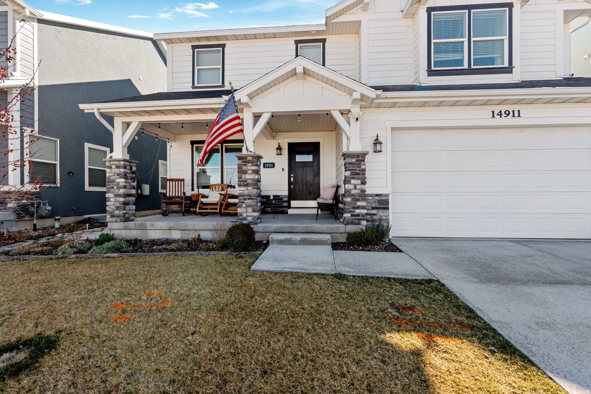 Property entrance with covered porch, a lawn, an attached garage, stone siding, and concrete driveway