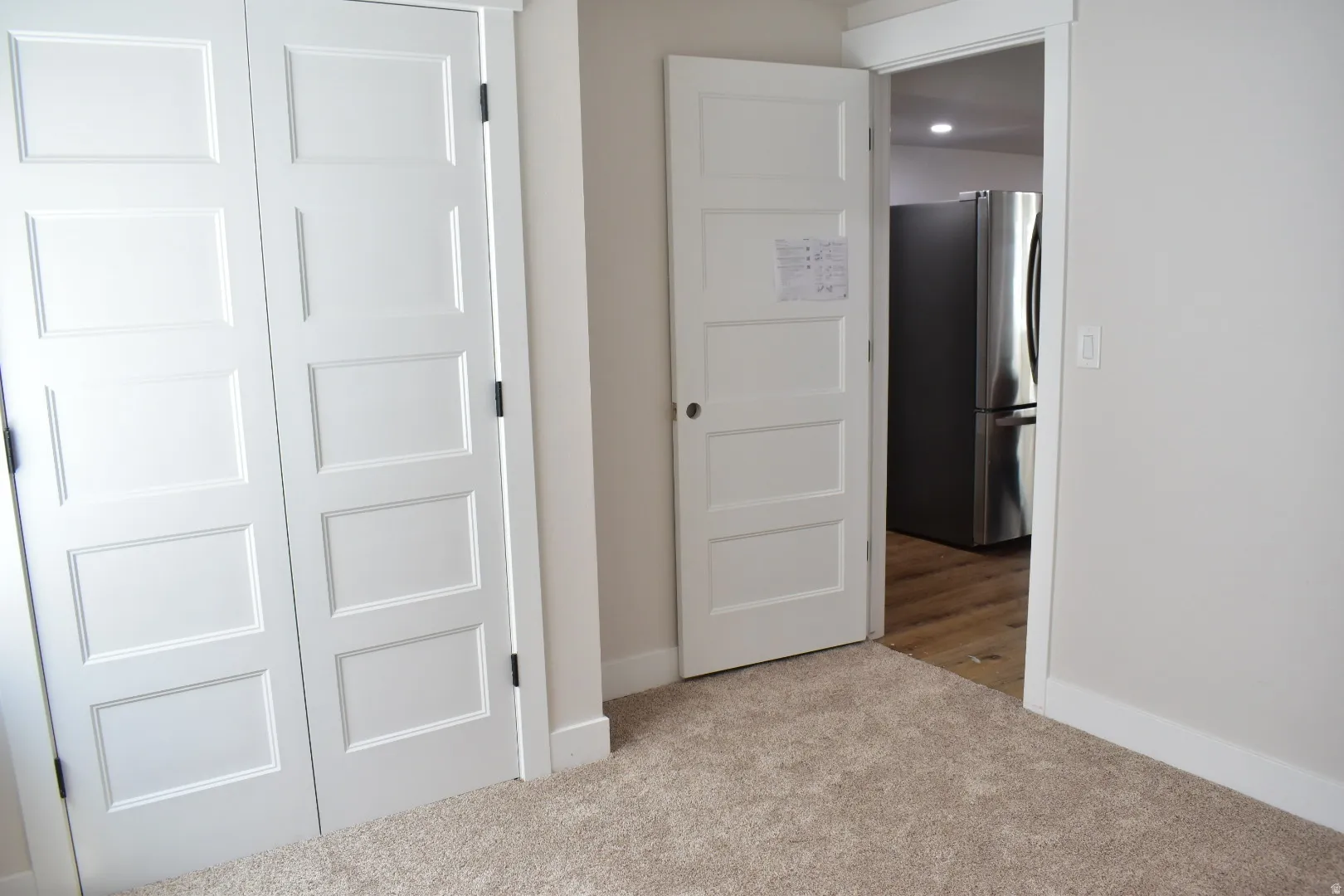 Unfurnished bedroom with freestanding refrigerator and light colored carpet