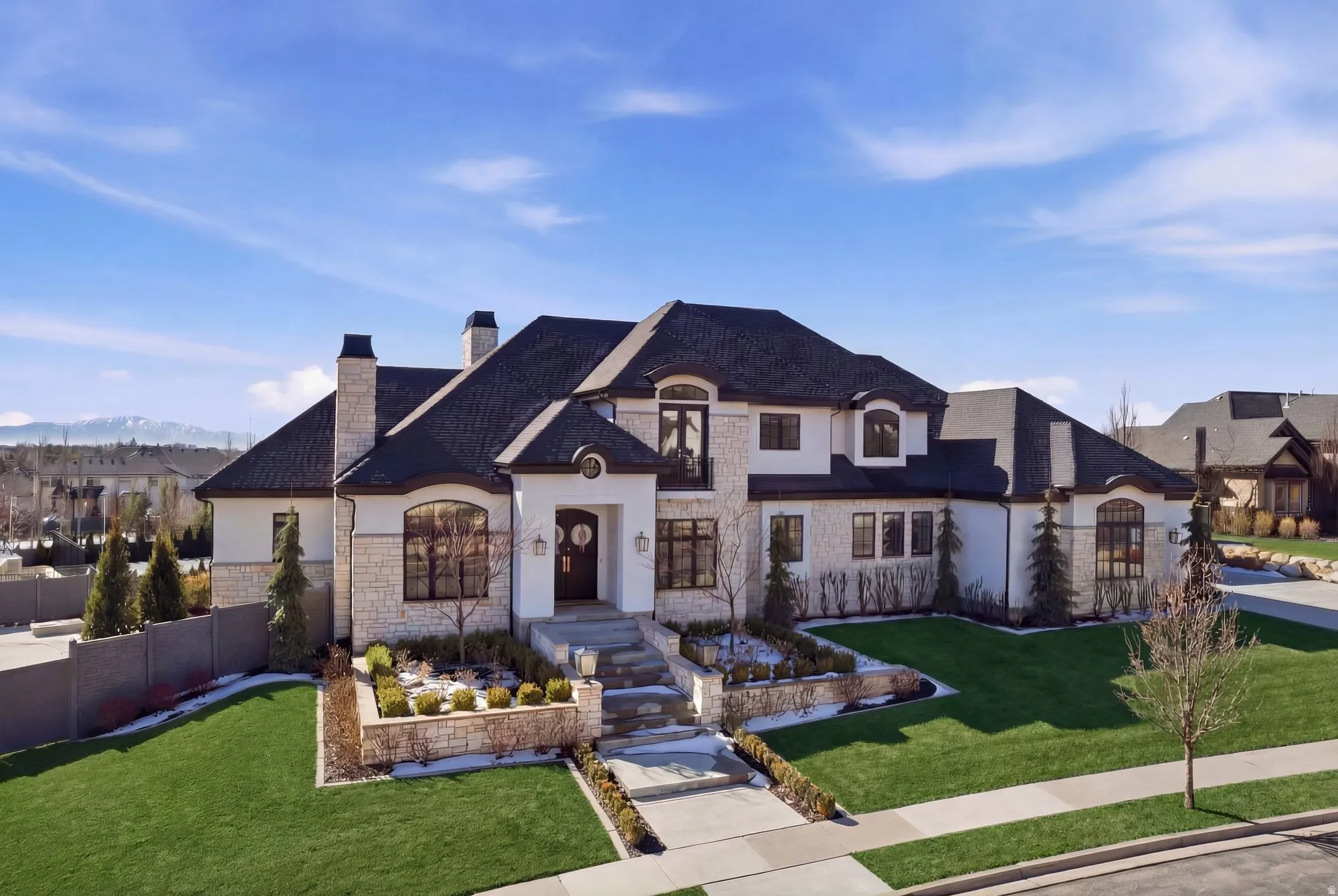 French country inspired facade featuring stucco siding, stone siding, a chimney, a front lawn, and a mountain view