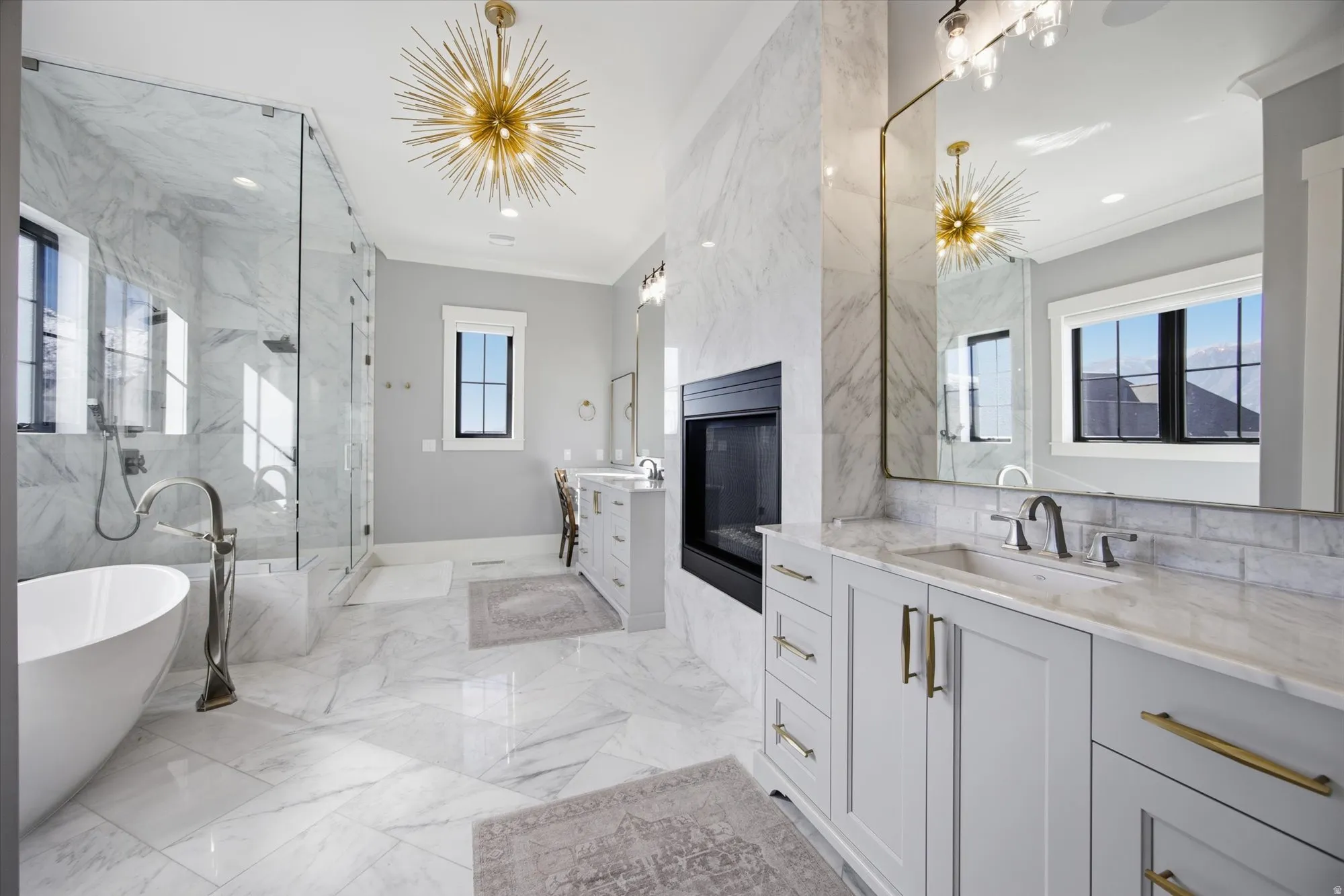Full bath with a freestanding tub, plenty of natural light, ornamental molding, two vanities, and a marble finish shower