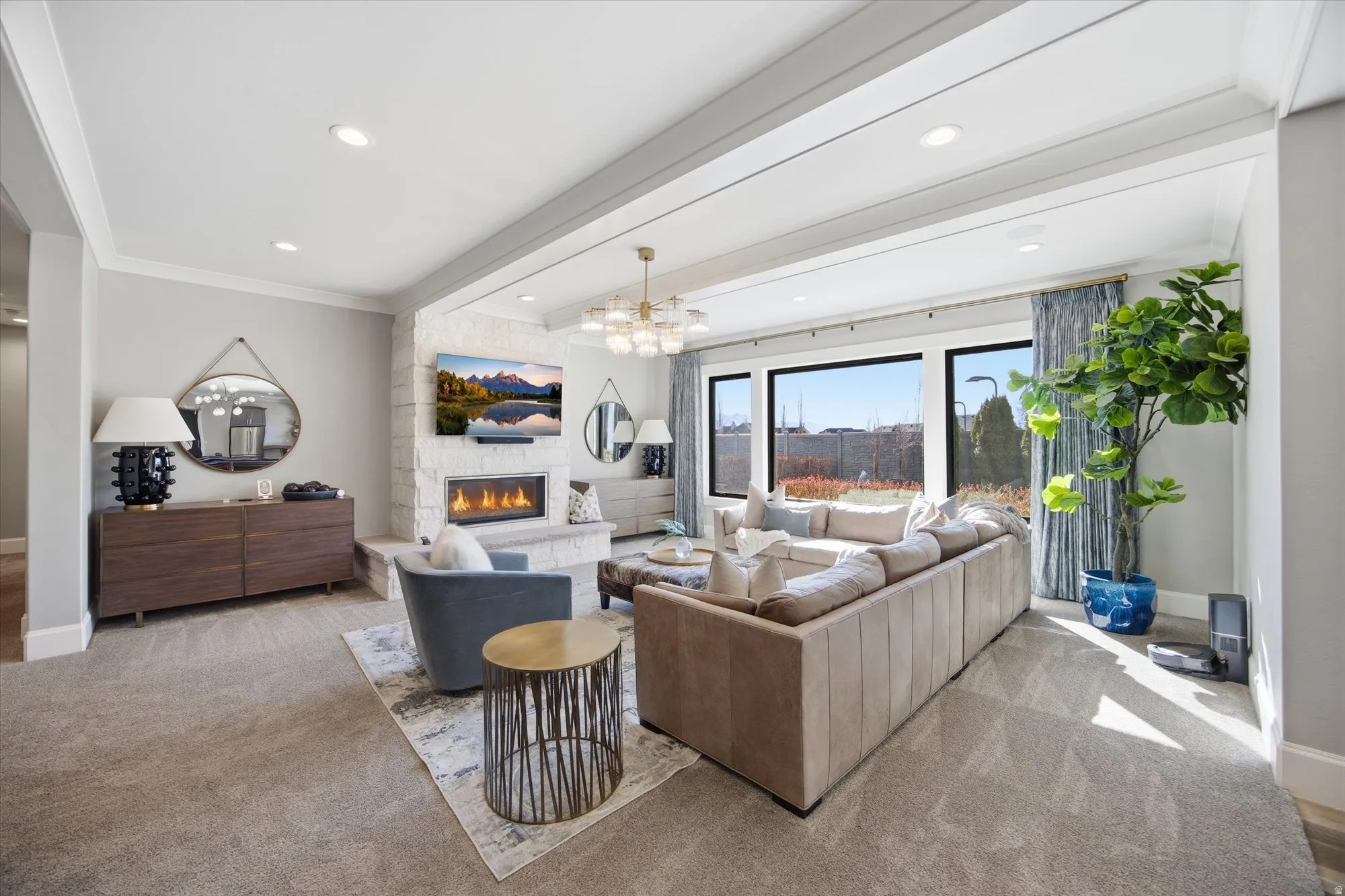 Carpeted living room with beam ceiling, a stone fireplace, hanging lights, and ornamental molding
