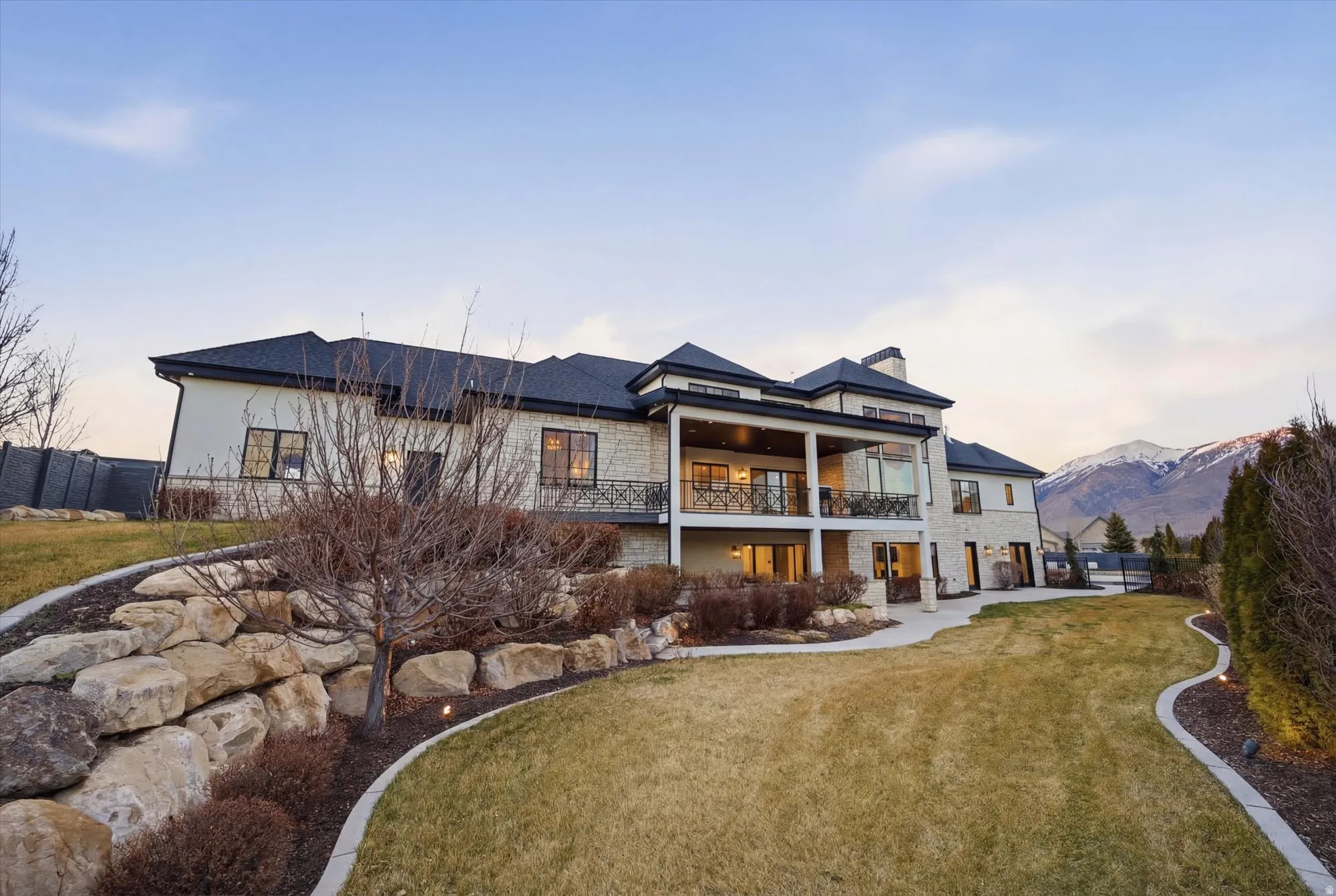 Back of house at dusk featuring a balcony, a chimney, stone siding, a patio, and a mountain view