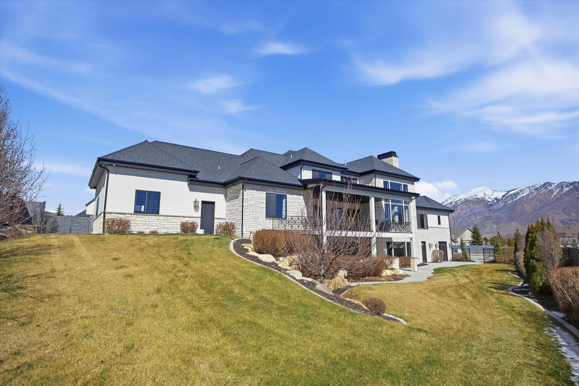 Back of property with a yard, a balcony, stone siding, a chimney, and a mountain view