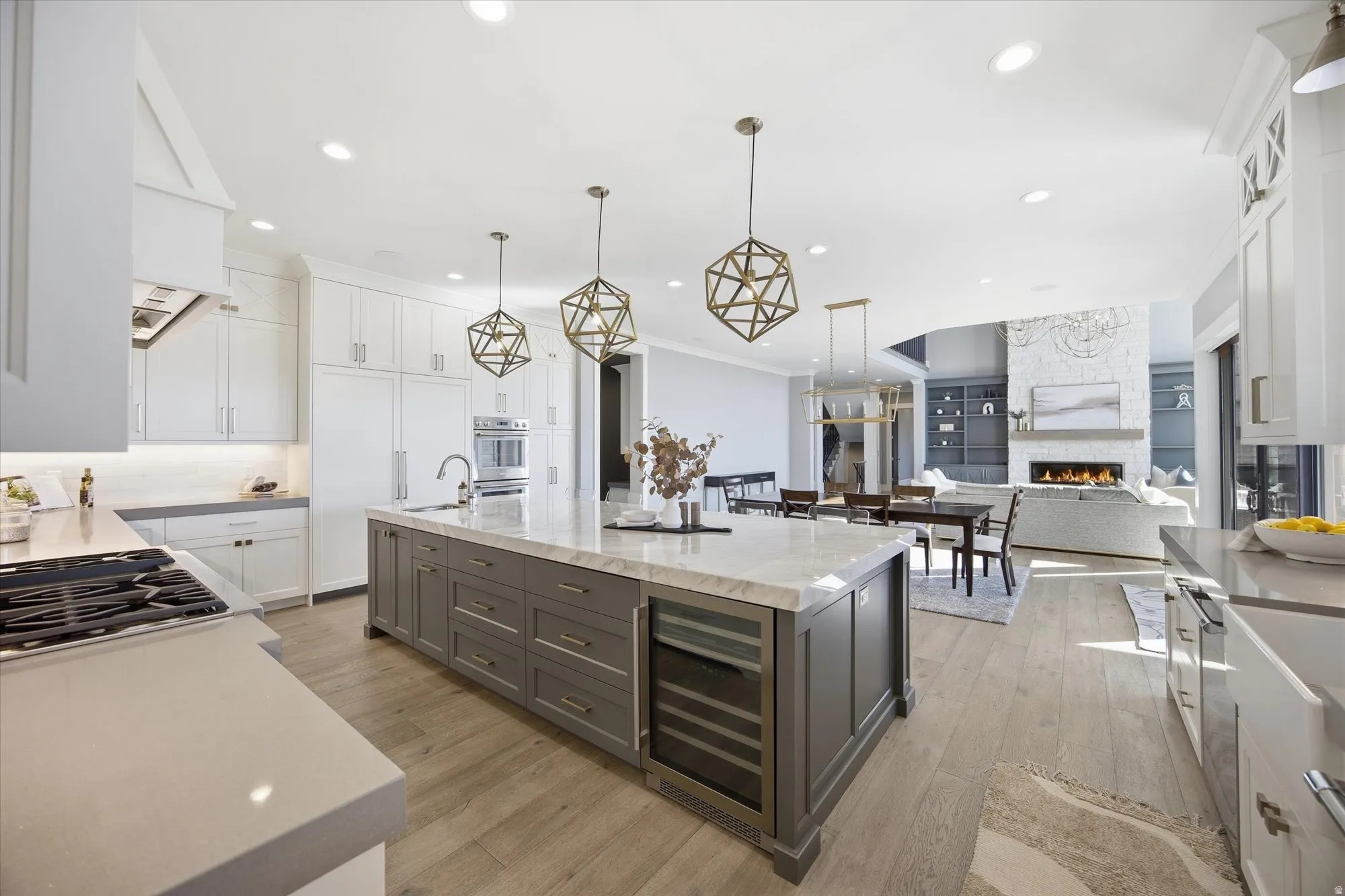 Kitchen with two tone cabinetry, a large fireplace, a large island with sink, wine cooler, and ornamental molding