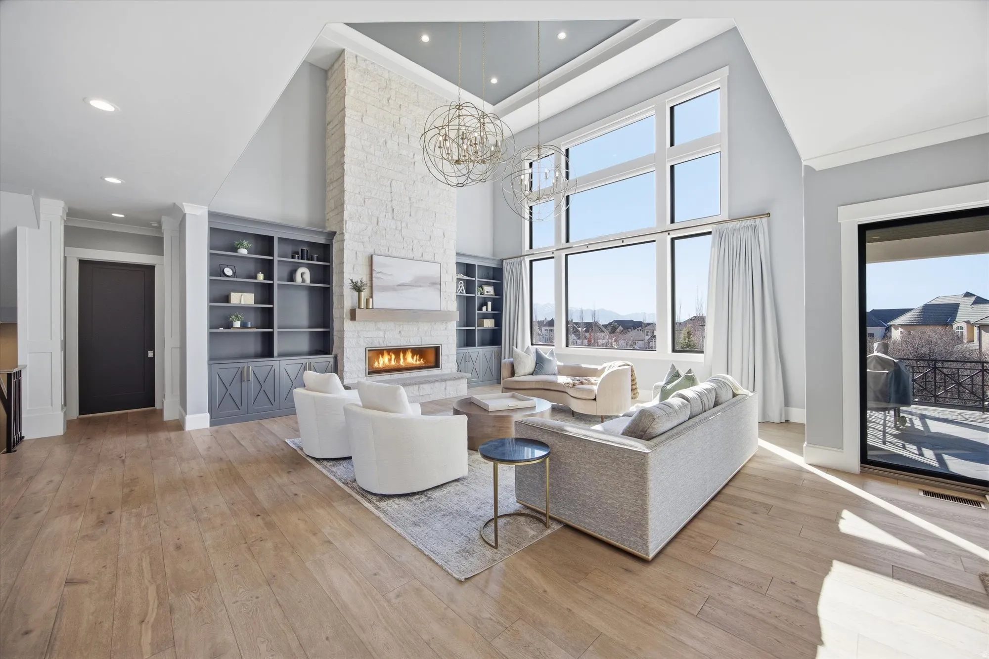 Living area featuring a high ceiling, light wood finished floors, a fireplace, suspended lighting, and built in features
