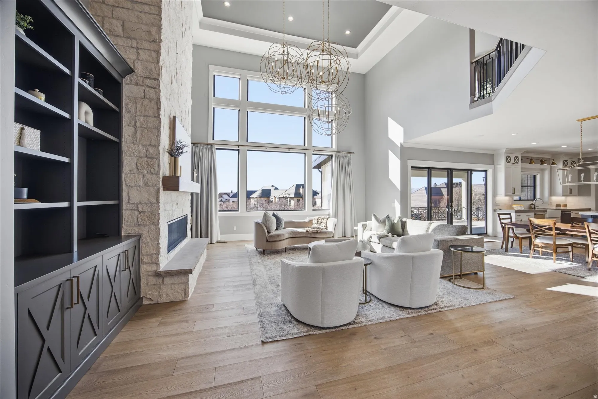 Living area with light wood finished floors, hanging lights, a stone fireplace, french doors, and a high ceiling