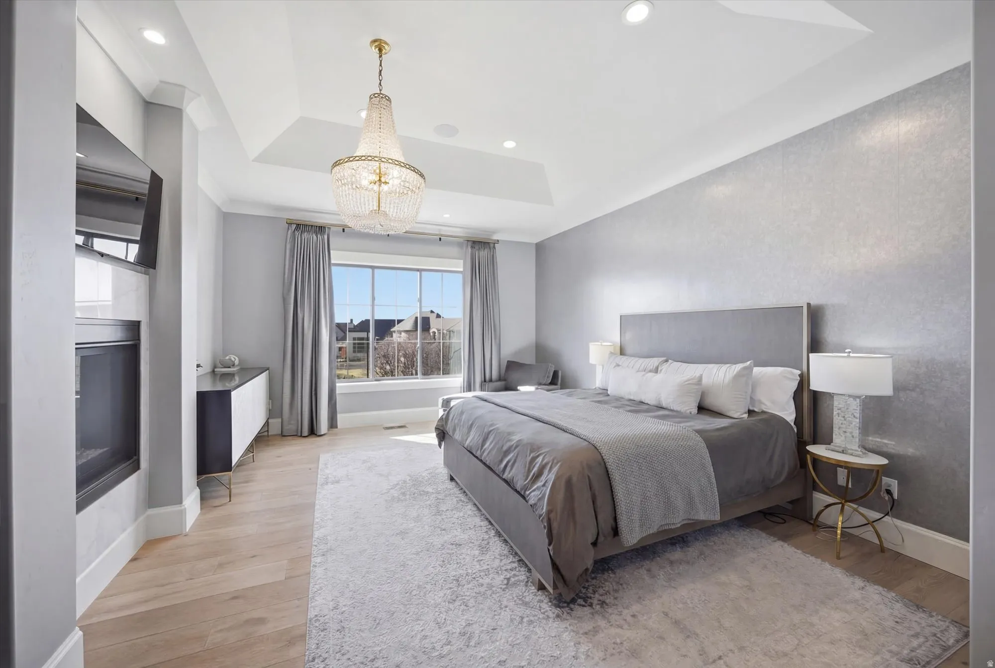 Bedroom featuring light wood-style flooring, suspended lighting, a raised ceiling, and a glass covered fireplace