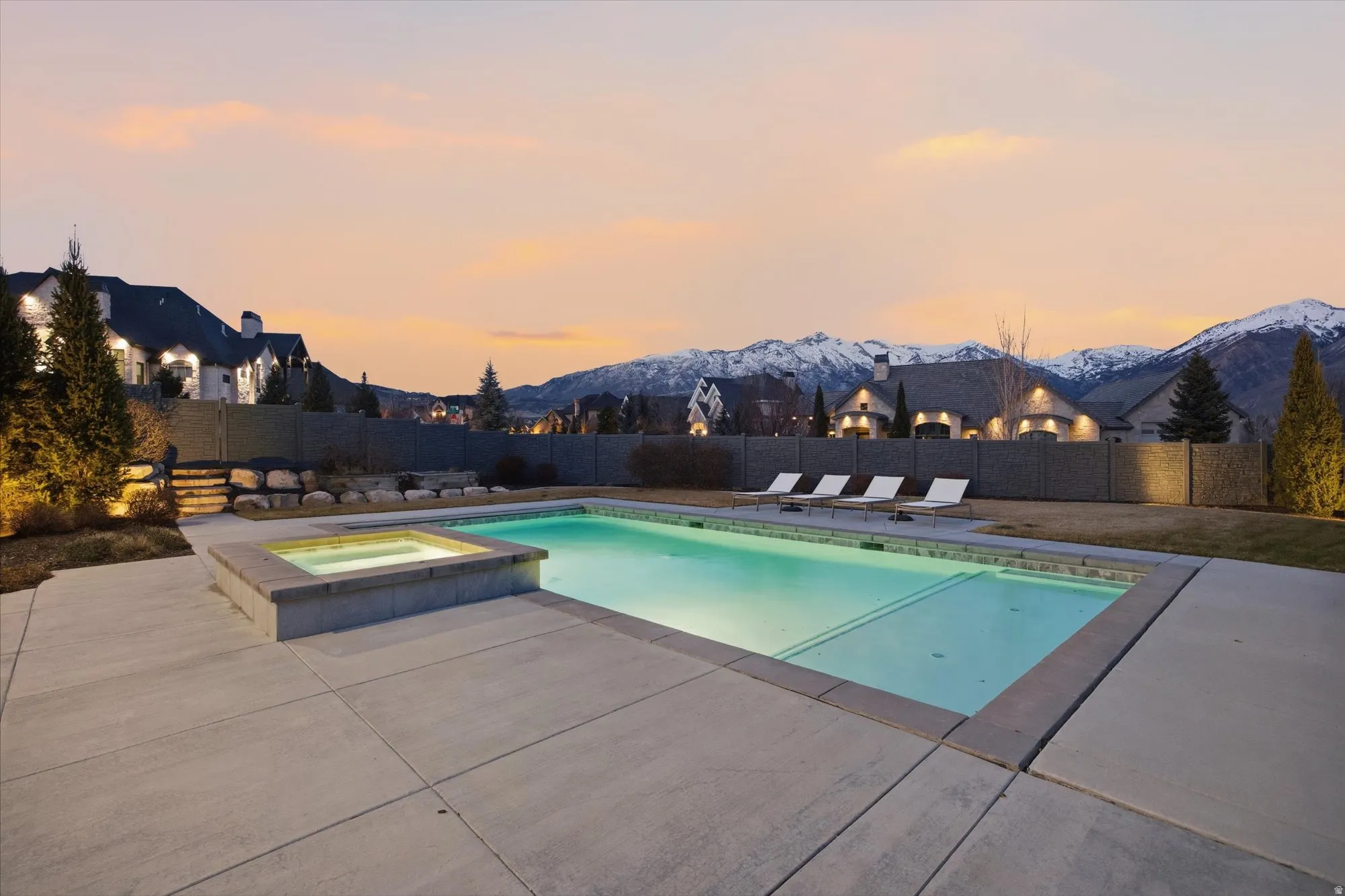 Pool at dusk with a fenced backyard, a patio, a pool with connected hot tub, and a mountain view