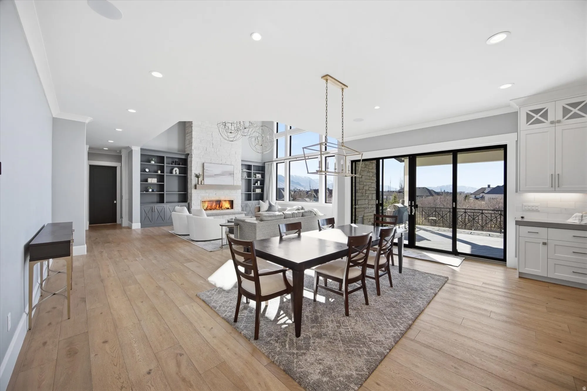 Dining area featuring crown molding, light wood-style flooring, a stone fireplace, hanging lights, and healthy amount of natural light