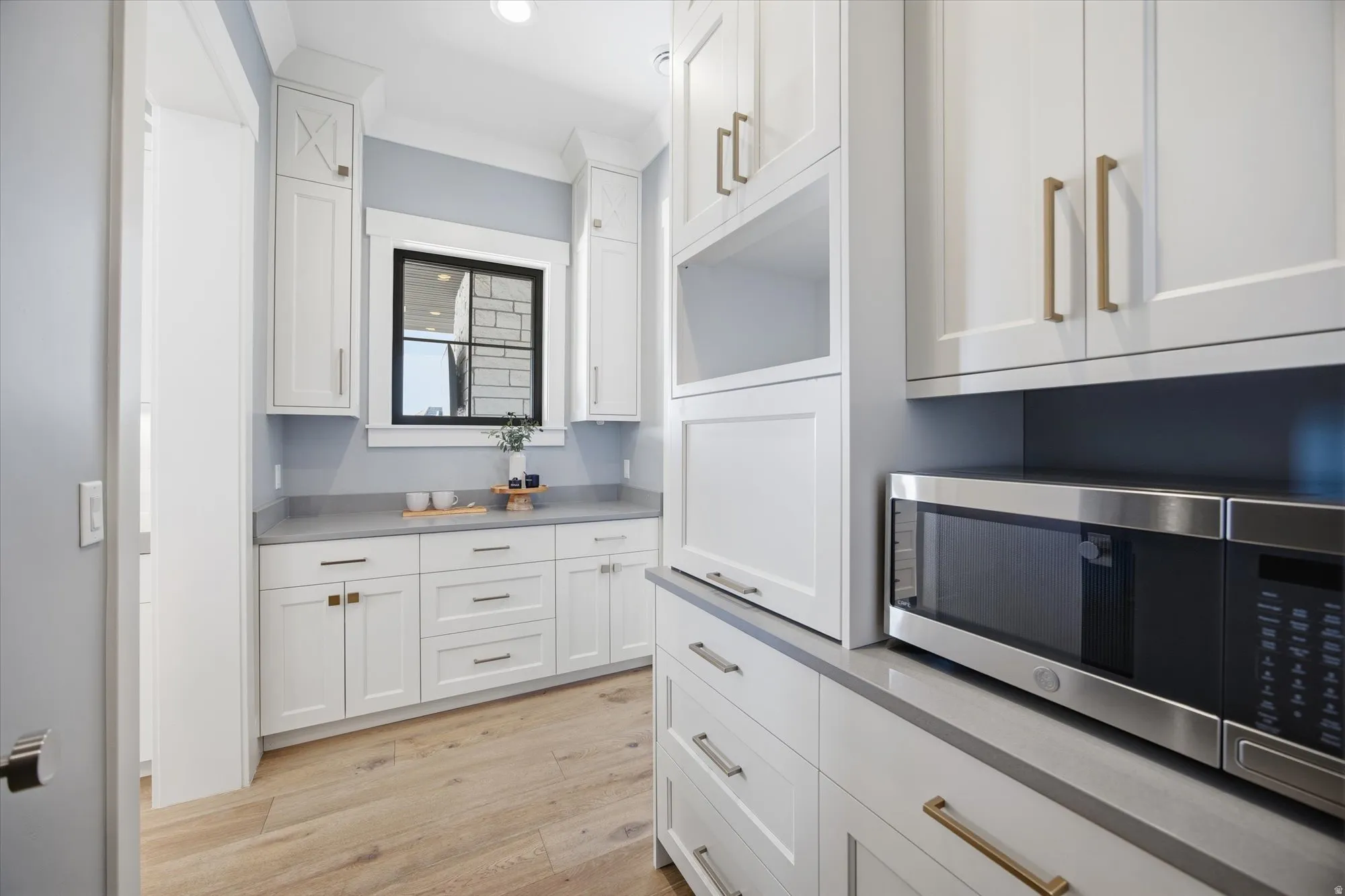 Kitchen with white cabinetry, stainless steel microwave, light wood-style flooring, and light countertops