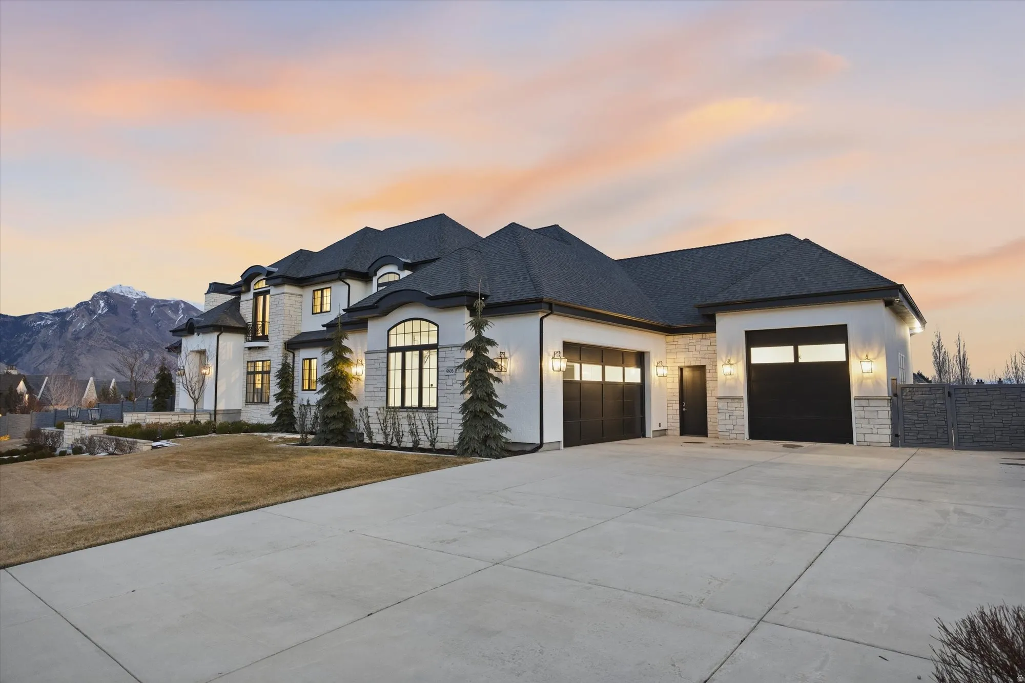 View of front of property featuring a garage, driveway, stone siding, and a shingled roof