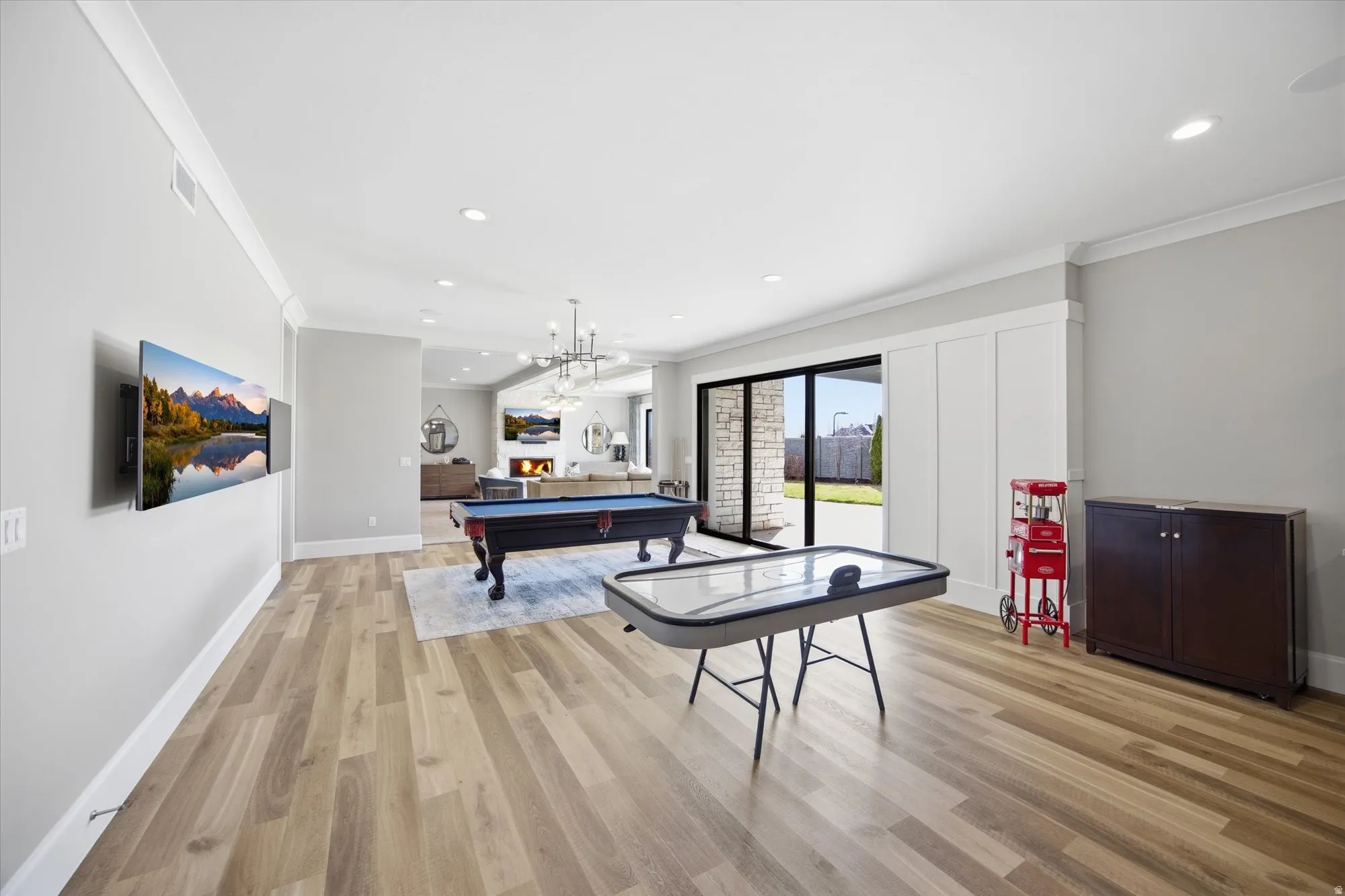Game room featuring ornamental molding, light wood-style flooring, billiards table, recessed lighting, and a warm lit fireplace