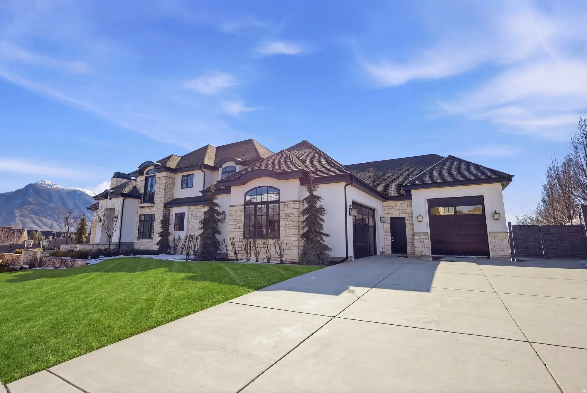 French country style house featuring a garage, stucco siding, concrete driveway, stone siding, and a mountain view
