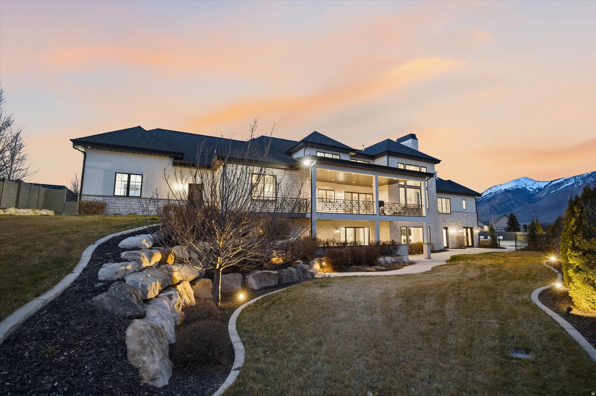 Back of property at dusk with a balcony, stone siding, a patio area, a mountain view, and a chimney