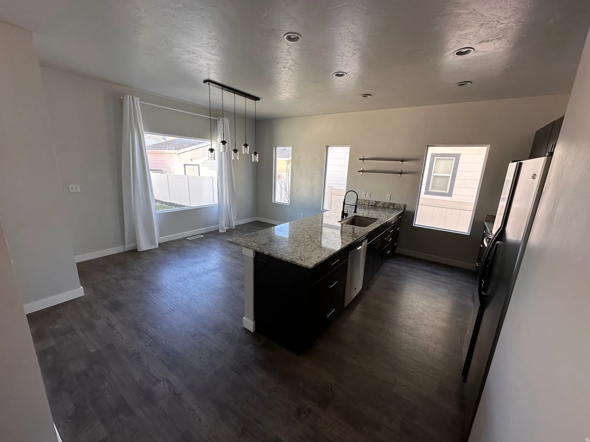 Kitchen featuring a peninsula, light stone countertops, stainless steel appliances, dark cabinets, and decorative light fixtures
