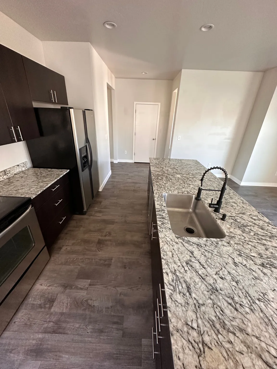 Kitchen featuring stainless steel appliances, dark wood finished floors, light stone counters, and recessed lighting