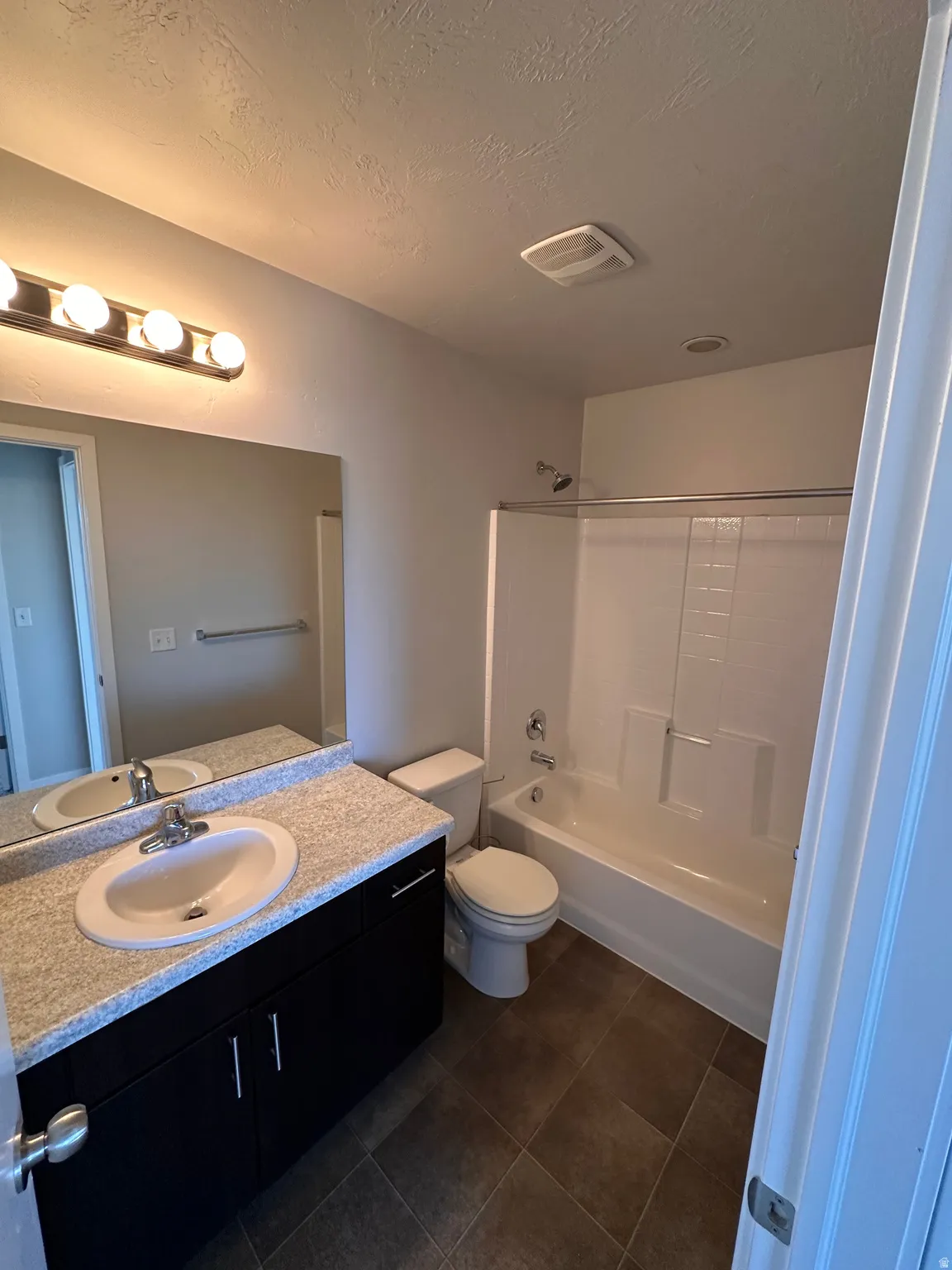 Bathroom with vanity, shower / bath combination, a textured ceiling, and dark tile patterned flooring