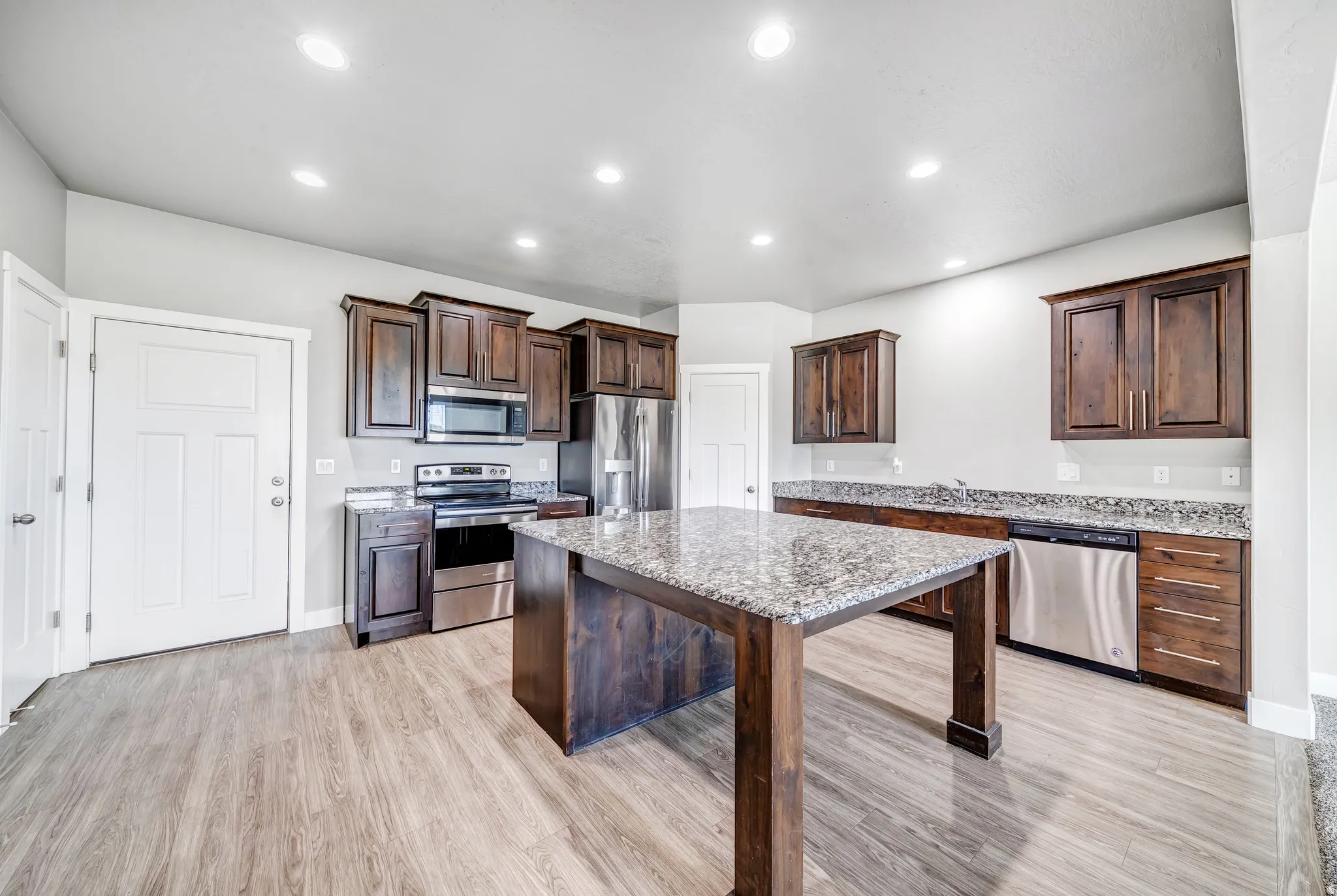 Kitchen featuring stainless steel appliances, dark wood finish cabinetry, light stone countertops, light wood-type flooring, and a kitchen island