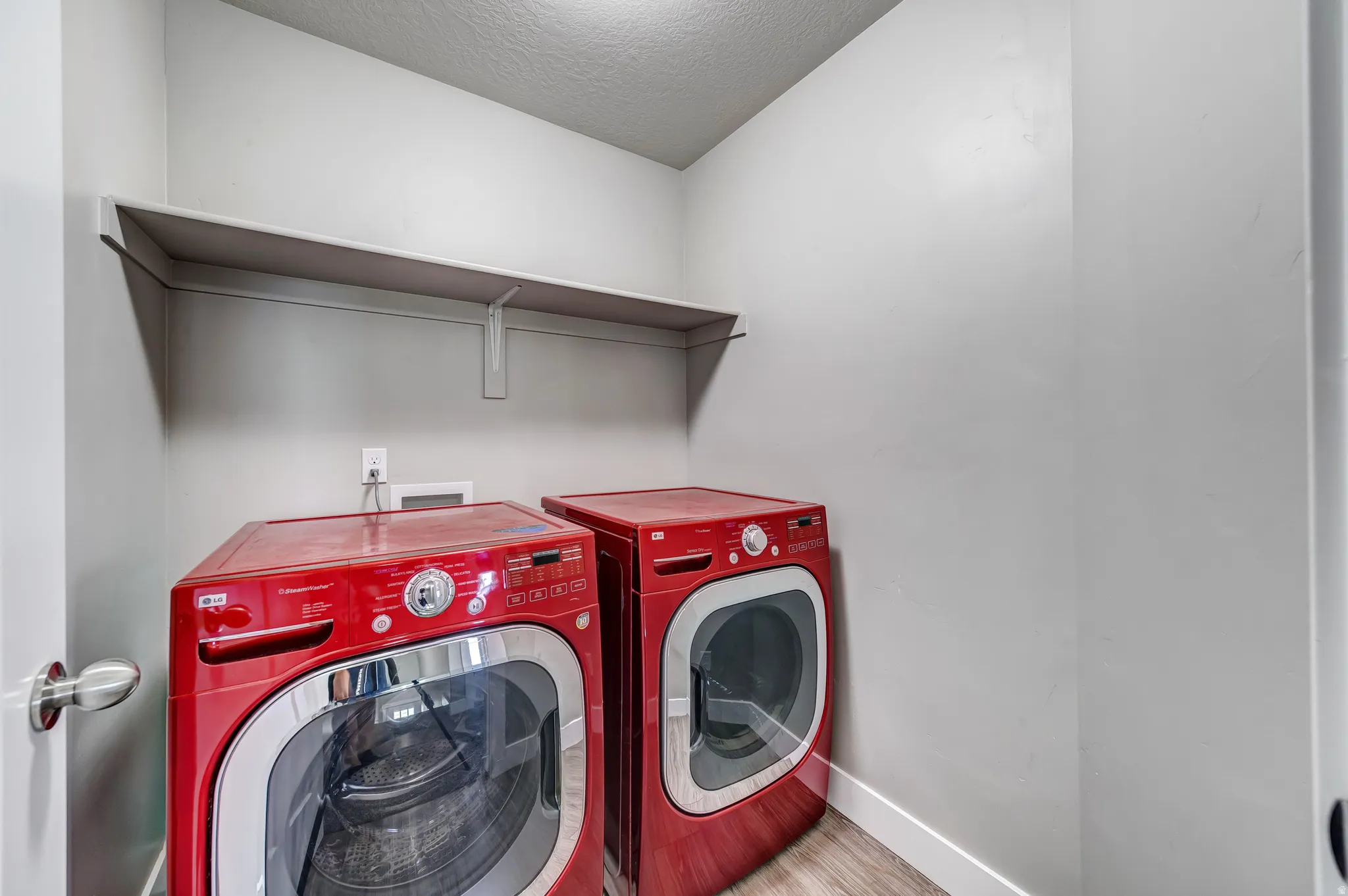 Laundry area featuring a textured ceiling, light wood-style floors, and washing machine and clothes dryer