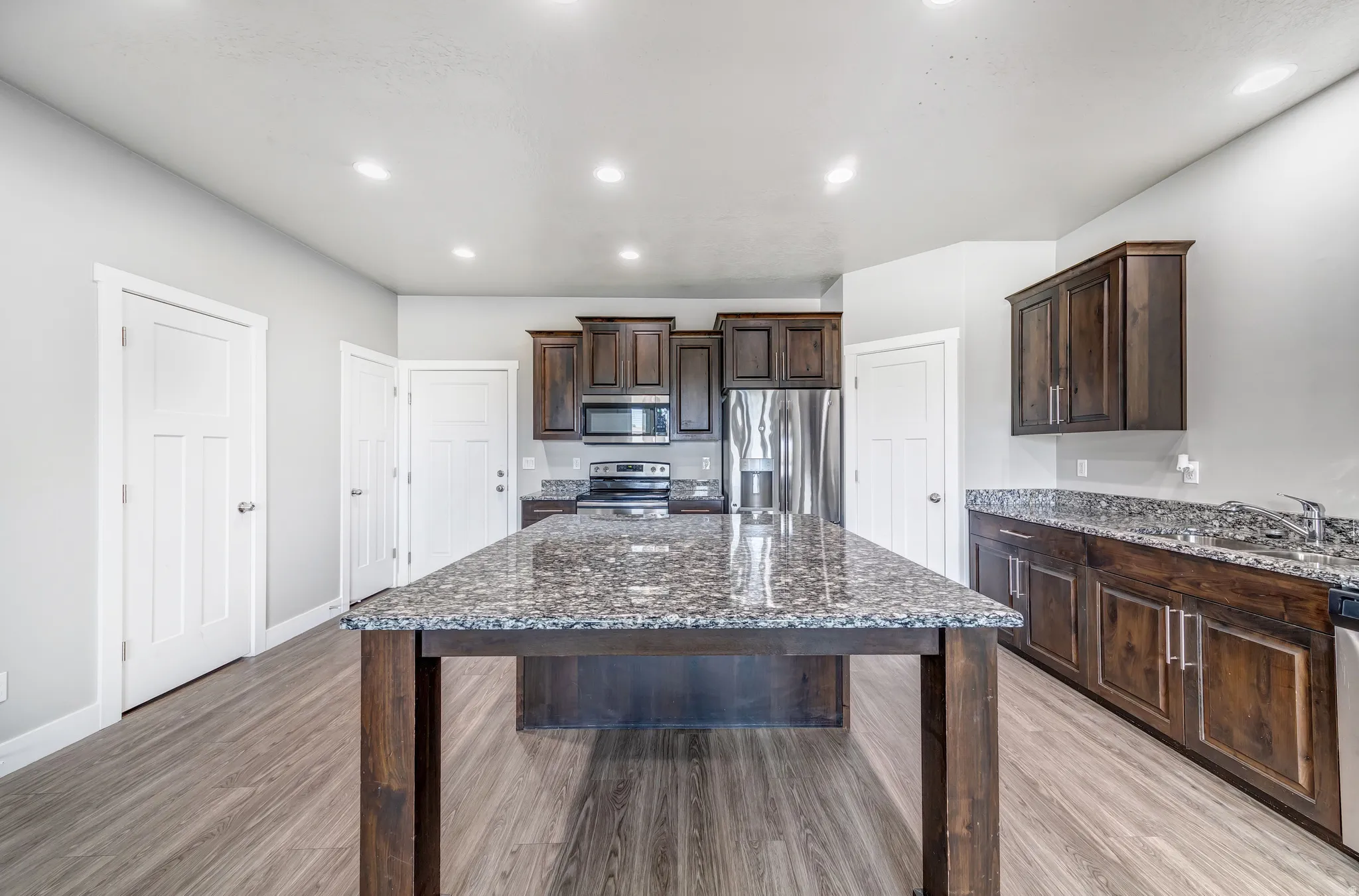 Kitchen with dark wood finish cabinetry, dark stone countertops, stainless steel appliances, a kitchen island, and light wood finished floors