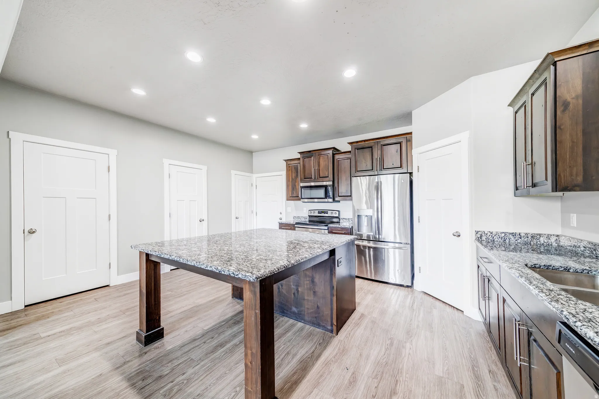 Kitchen with dark wood finish cabinets, light stone counters, stainless steel appliances, light wood-style flooring, and recessed lighting