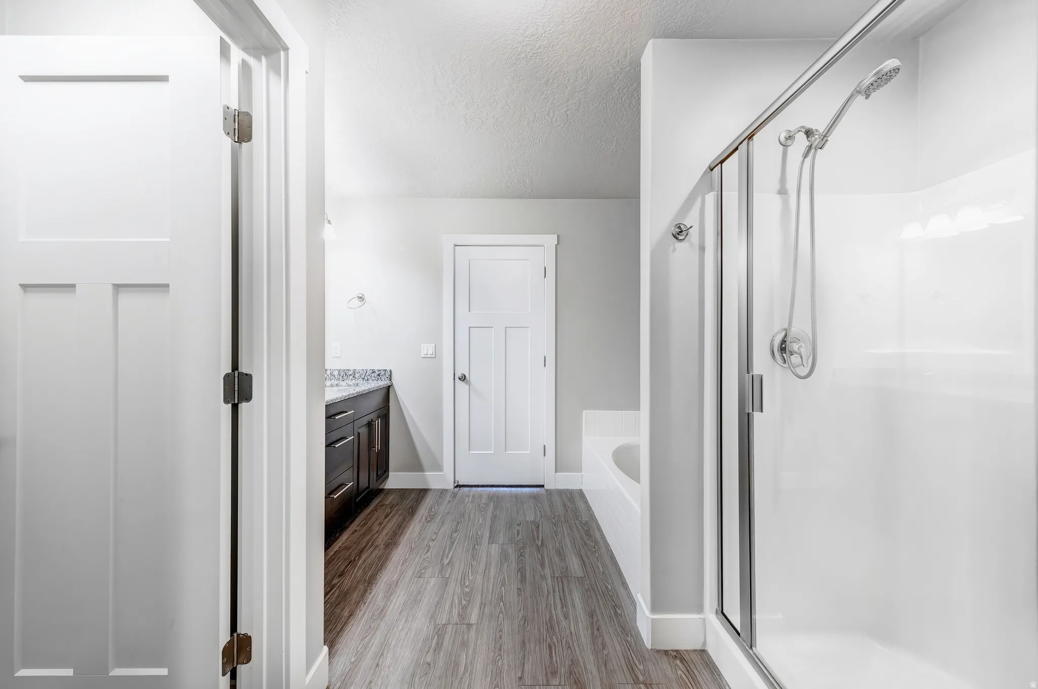 Full bath featuring vanity, a garden tub, a textured ceiling, a stall shower, and light wood-style floors
