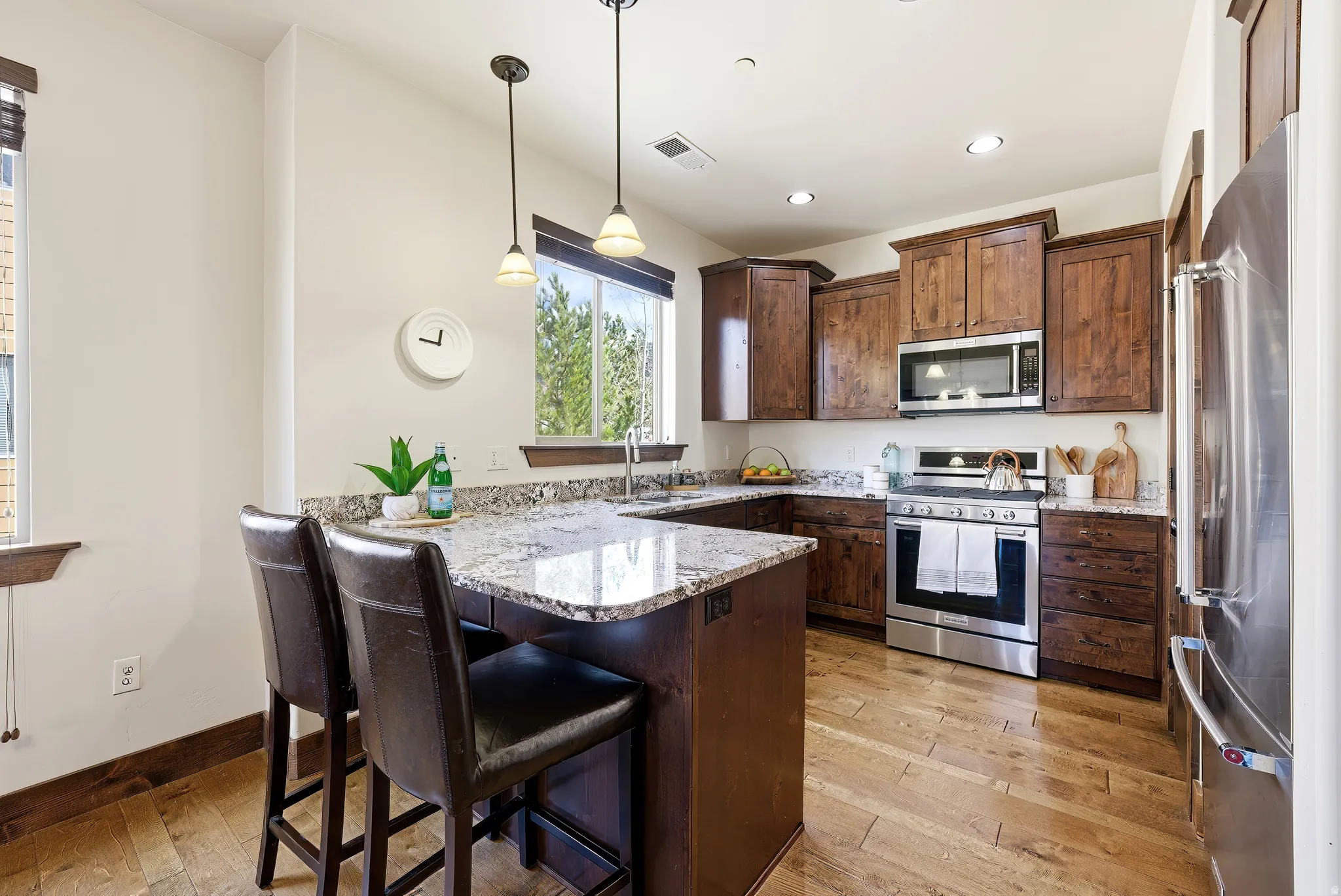 Kitchen with a breakfast bar, stainless steel appliances, a peninsula, light granite countertops, and wood flooring