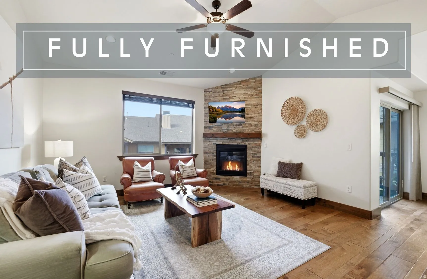Living room with vaulted ceiling, a stone fireplace, hardwood / wood-style flooring, and ceiling fan