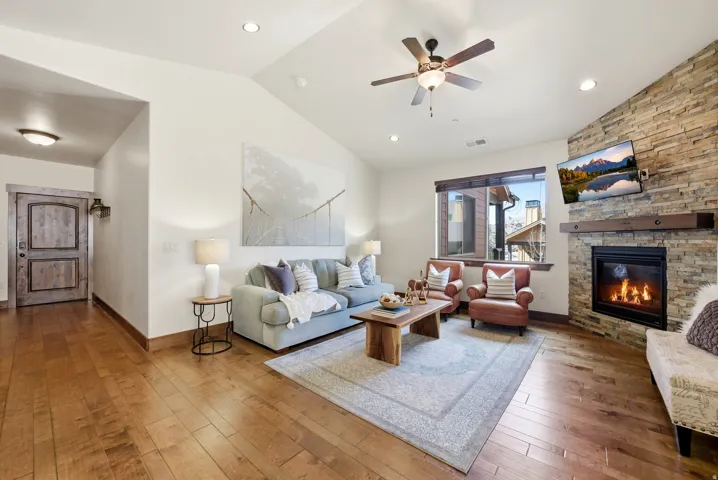 Fully furnished living area featuring a stone fireplace, hardwood / wood-style flooring, a ceiling fan, lofted ceiling, and recessed lighting