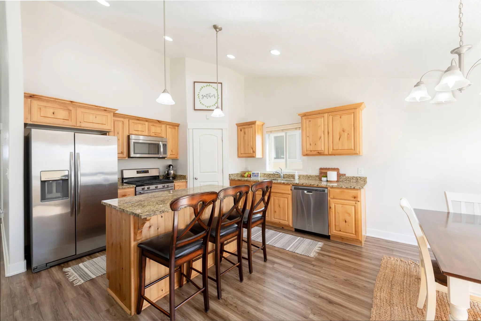 Kitchen featuring light stone countertops, stainless steel appliances, hanging lights, a kitchen breakfast bar, and light wood-style flooring