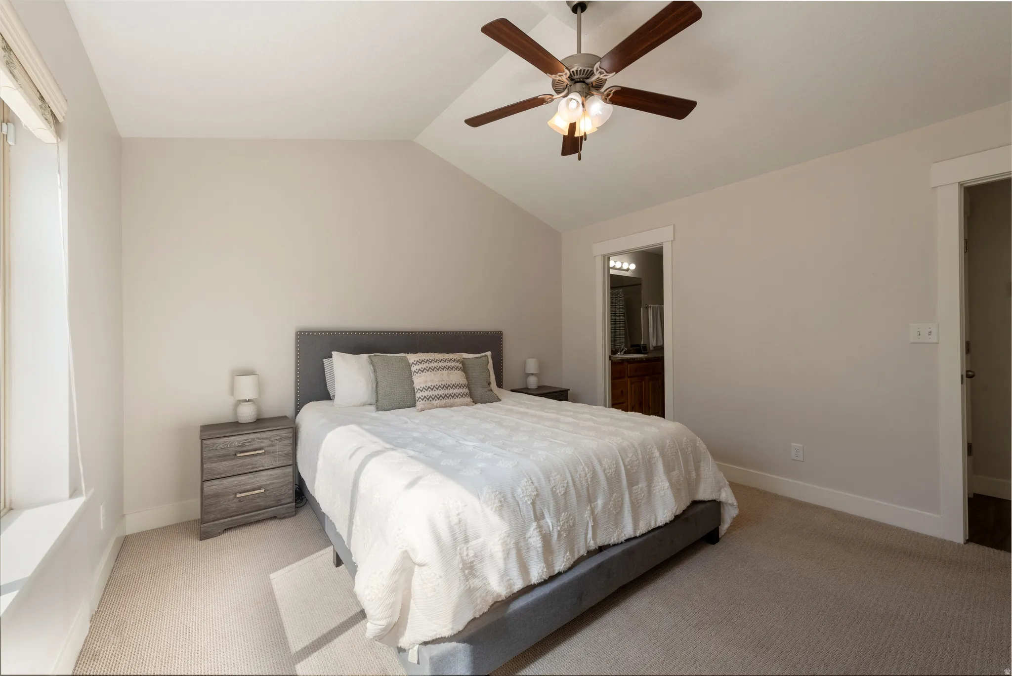 Bedroom featuring vaulted ceiling, carpet, ceiling fan, and ensuite bath