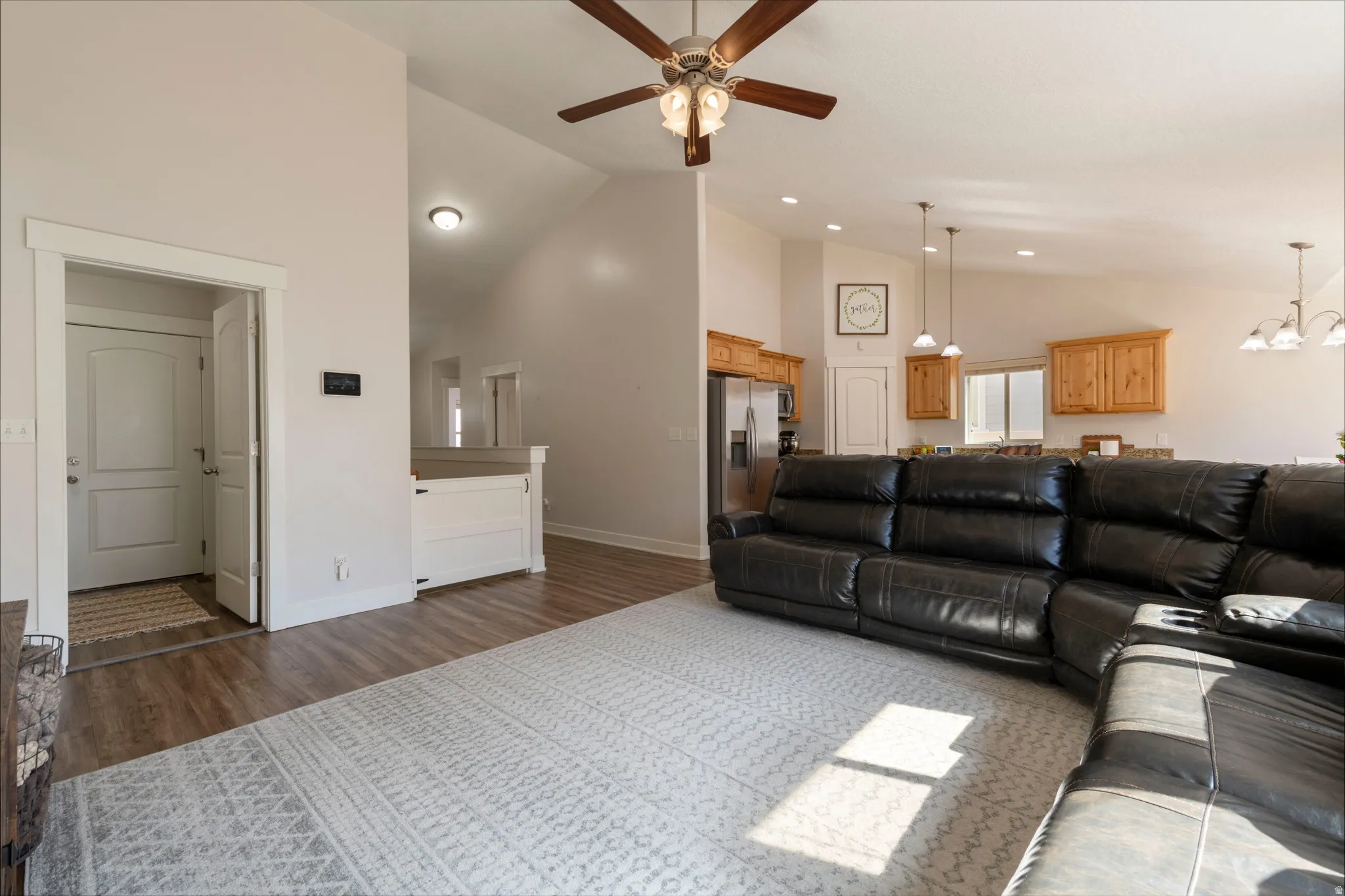 Living room featuring dark wood-style flooring, ceiling fan, lofted ceiling, and a chandelier