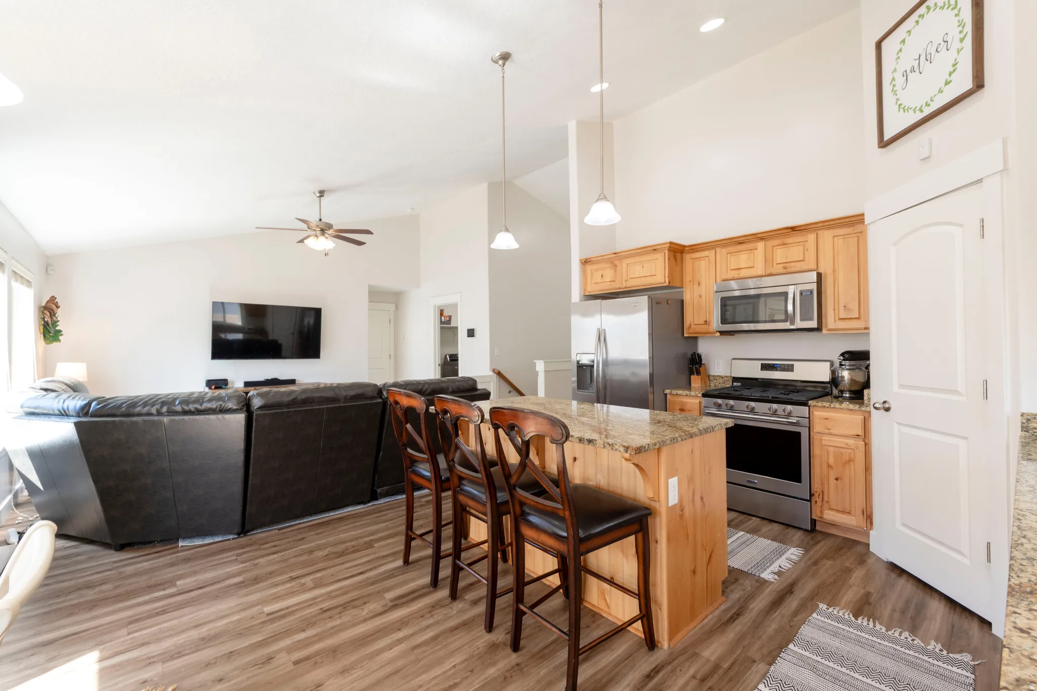 Kitchen featuring stainless steel appliances, a kitchen bar, open floor plan, light stone countertops, and lofted ceiling