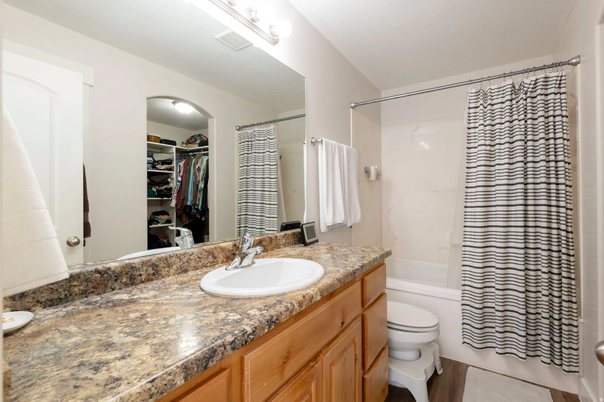 Full bathroom with a spacious closet, vanity, shower / bathtub combination with curtain, and light wood finished floors