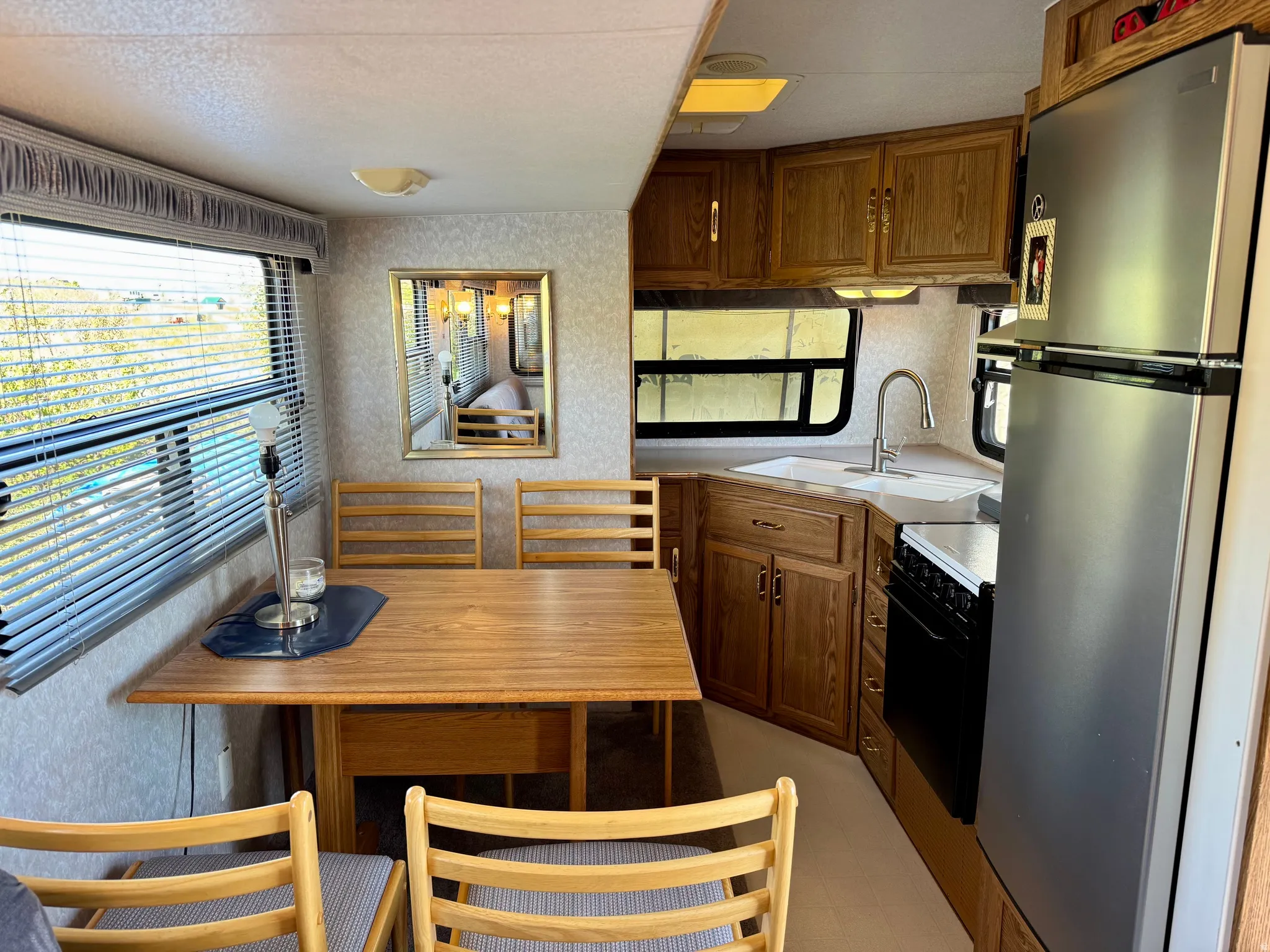 Compact kitchen and dining area featuring wood-finish cabinetry, a stainless steel refrigerator, a built-in range, a single basin sink, and a wood-finish dining table with matching chairs