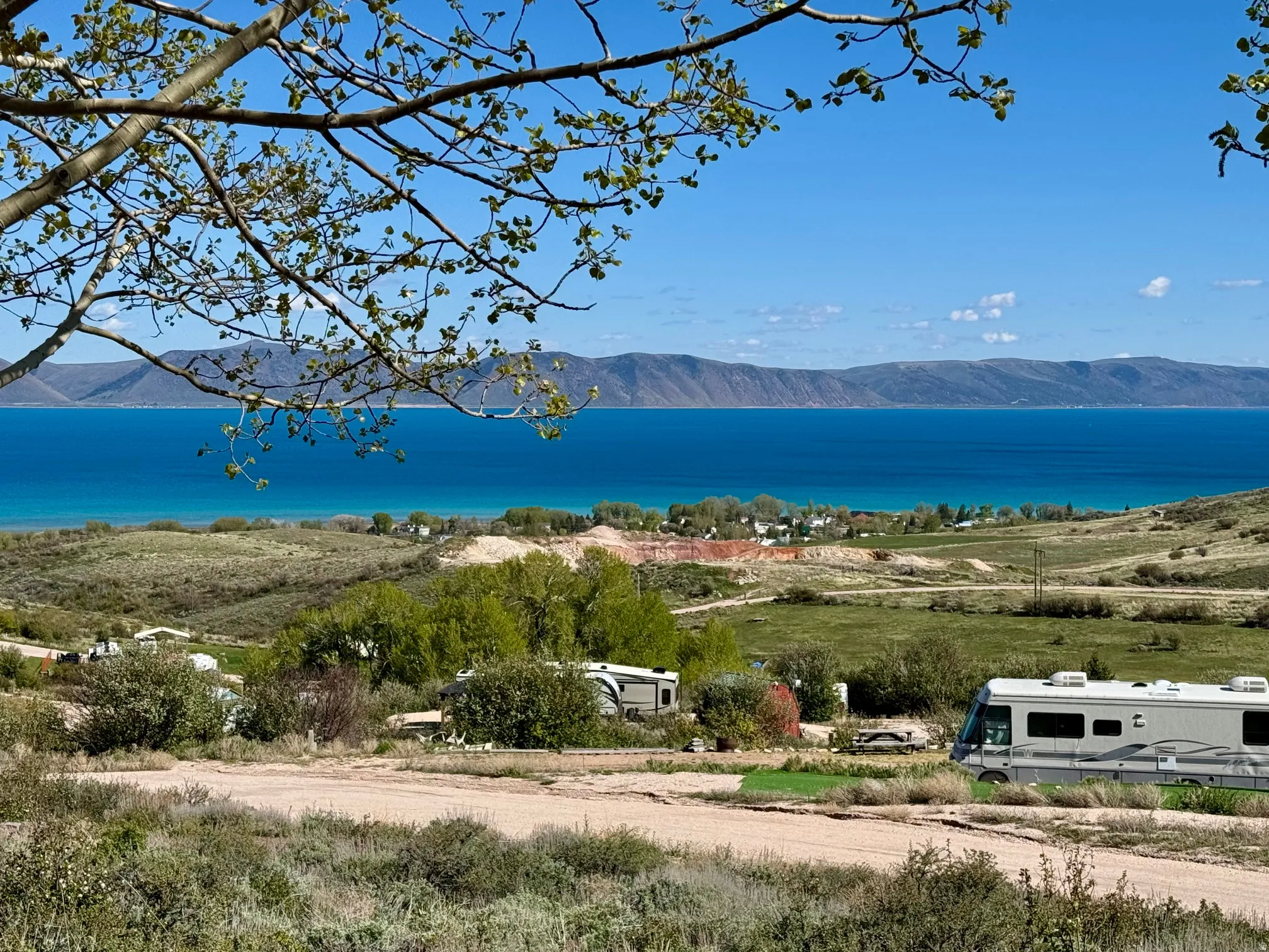 Expansive natural landscape featuring a prominent blue body of water, distant mountain ranges, and verdant green foliage