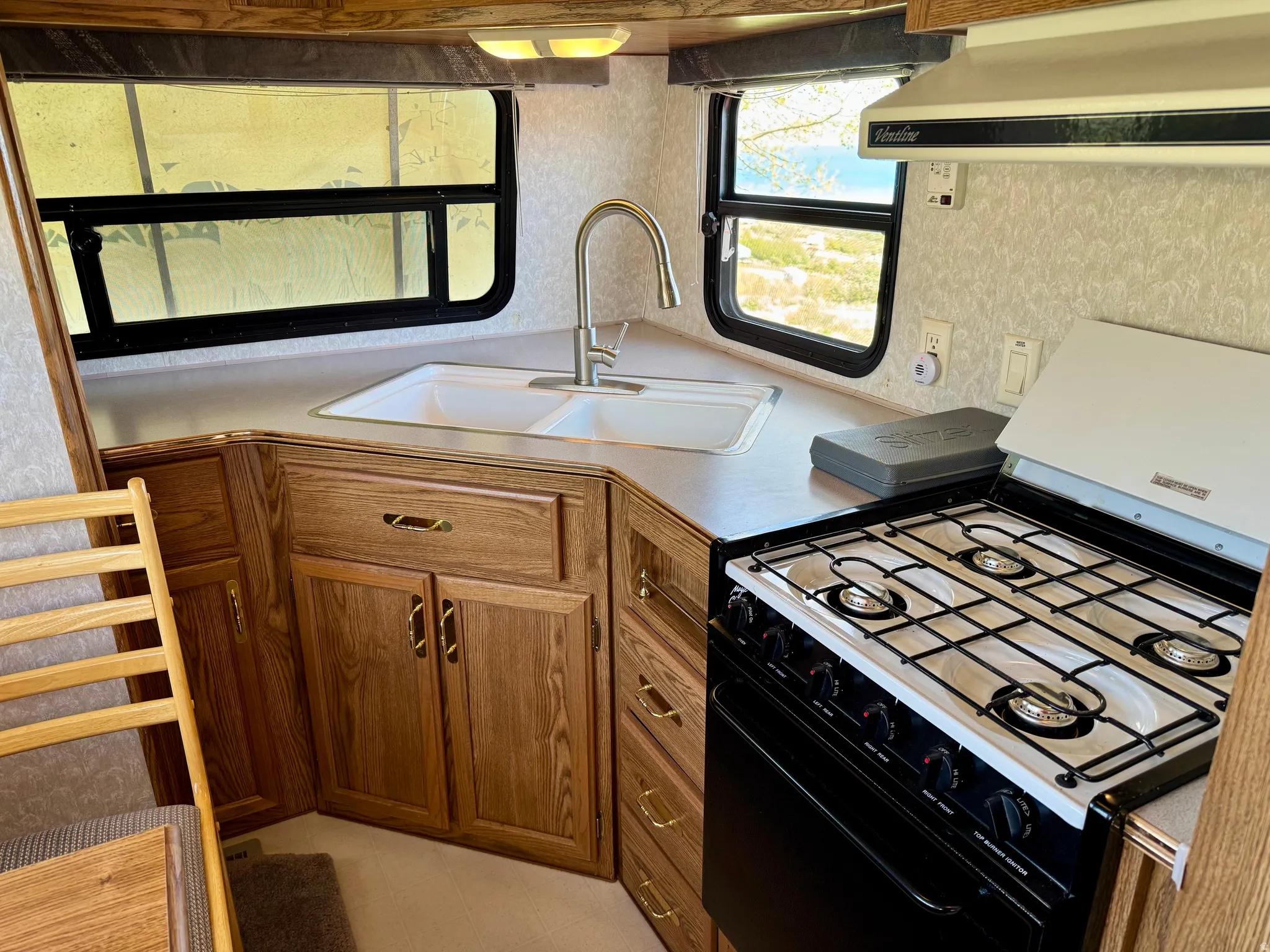 Compact kitchen featuring wood-finish cabinetry and a dual-basin sink with a gooseneck faucet