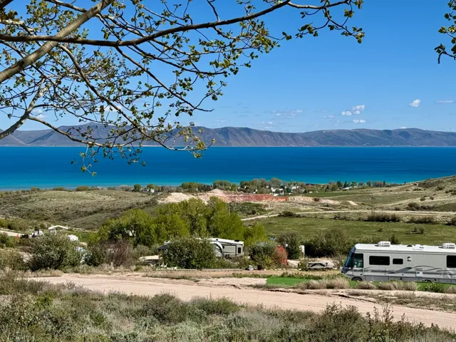 Expansive natural landscape featuring a prominent blue body of water, distant mountain ranges, and verdant green foliage