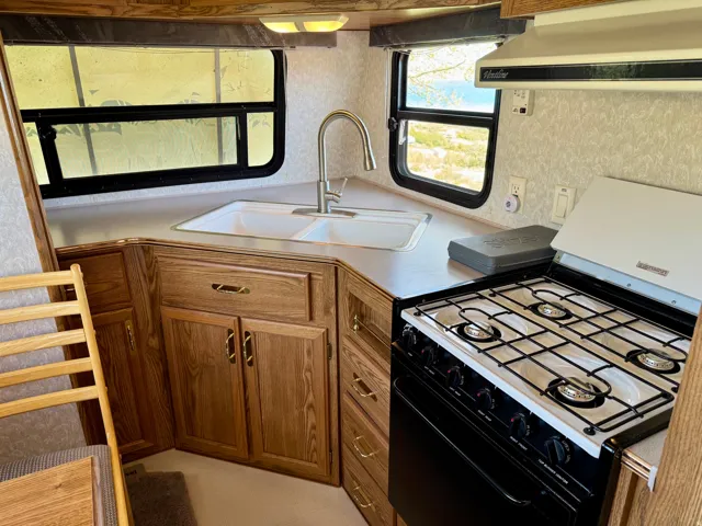Compact kitchen featuring wood-finish cabinetry and a dual-basin sink with a gooseneck faucet