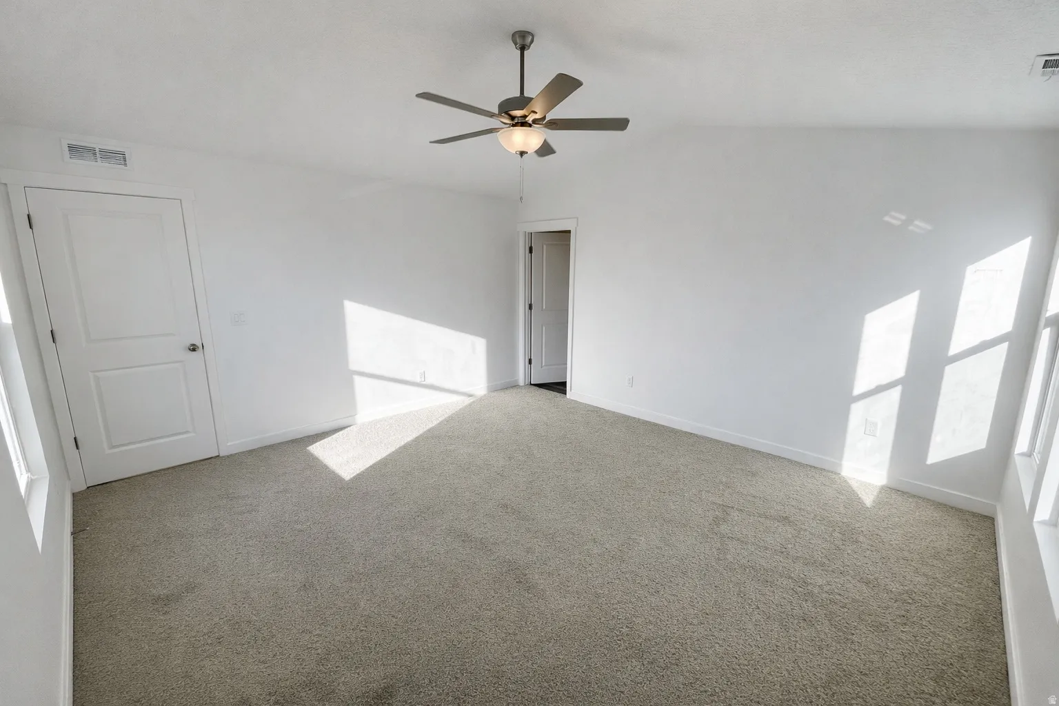 Spare room featuring light colored carpet, ceiling fan, and vaulted ceiling