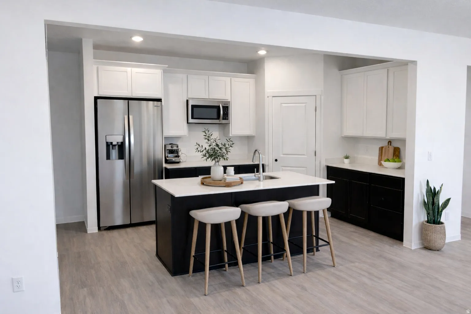 Kitchen with two tone cabinets, stainless steel appliances, a breakfast bar area, light wood-style flooring, and a center island with sink