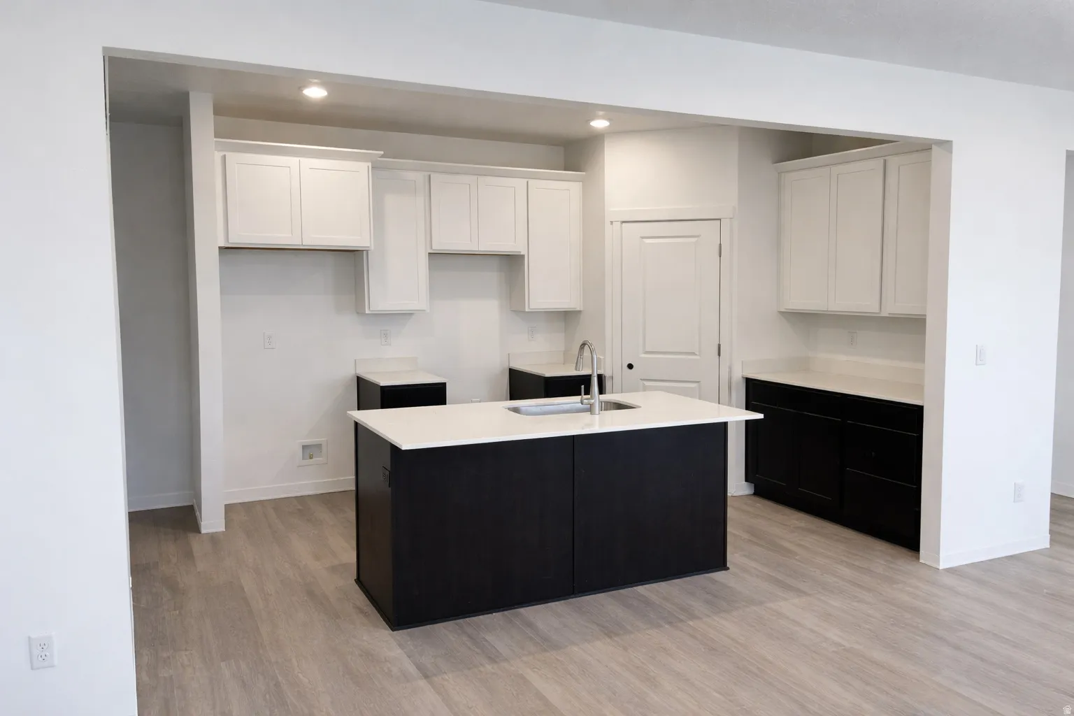 Kitchen featuring two tone color scheme, light wood-style floors, recessed lighting, light stone counters, and a kitchen island with sink