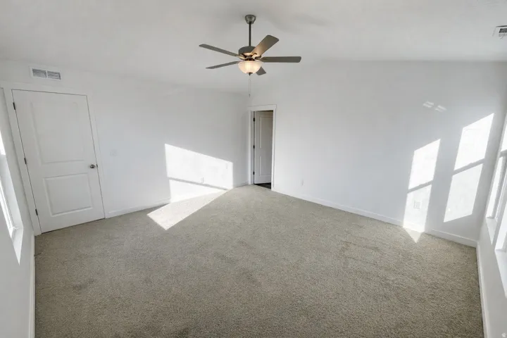 Spare room featuring light colored carpet, ceiling fan, and vaulted ceiling