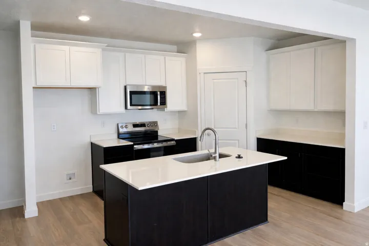 Dual tone kitchen with dual tone cabinetry, stainless steel appliances, a center island with sink, light wood-type flooring, and recessed lighting