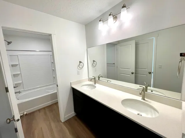 Full bathroom with a textured ceiling, double vanity, dark wood-style flooring, and shower / washtub combination