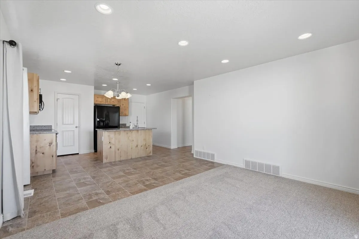 Kitchen with a kitchen island with sink, light wood finish cabinetry, a chandelier, light stone countertops, and stone finish flooring